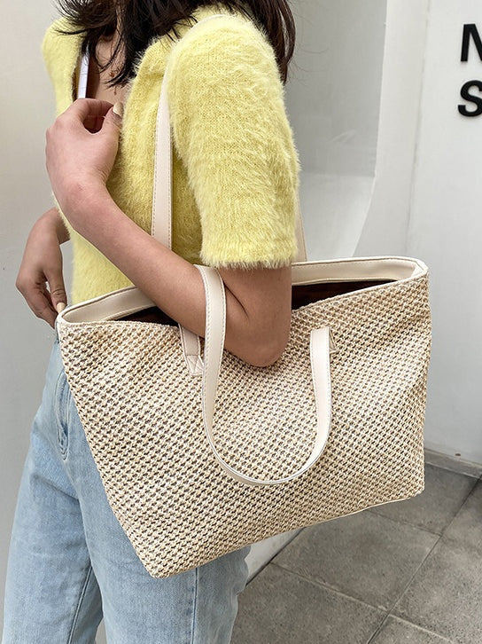 A model carries a medium cream woven tote over her shoulder, showing its structured rectangular silhouette, open top, textured construction, and long matching straps.