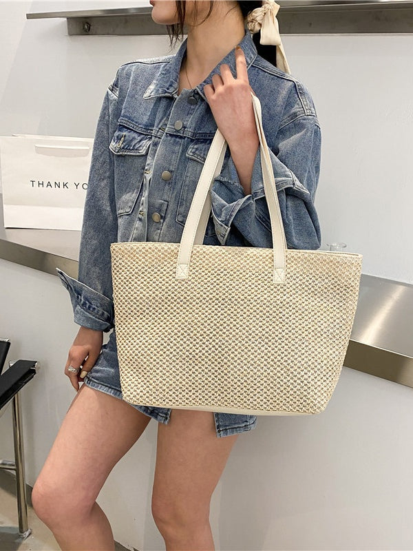 A model holds a cream woven tote bag by its long shoulder straps, showcasing the medium structured rectangular silhouette and open top.