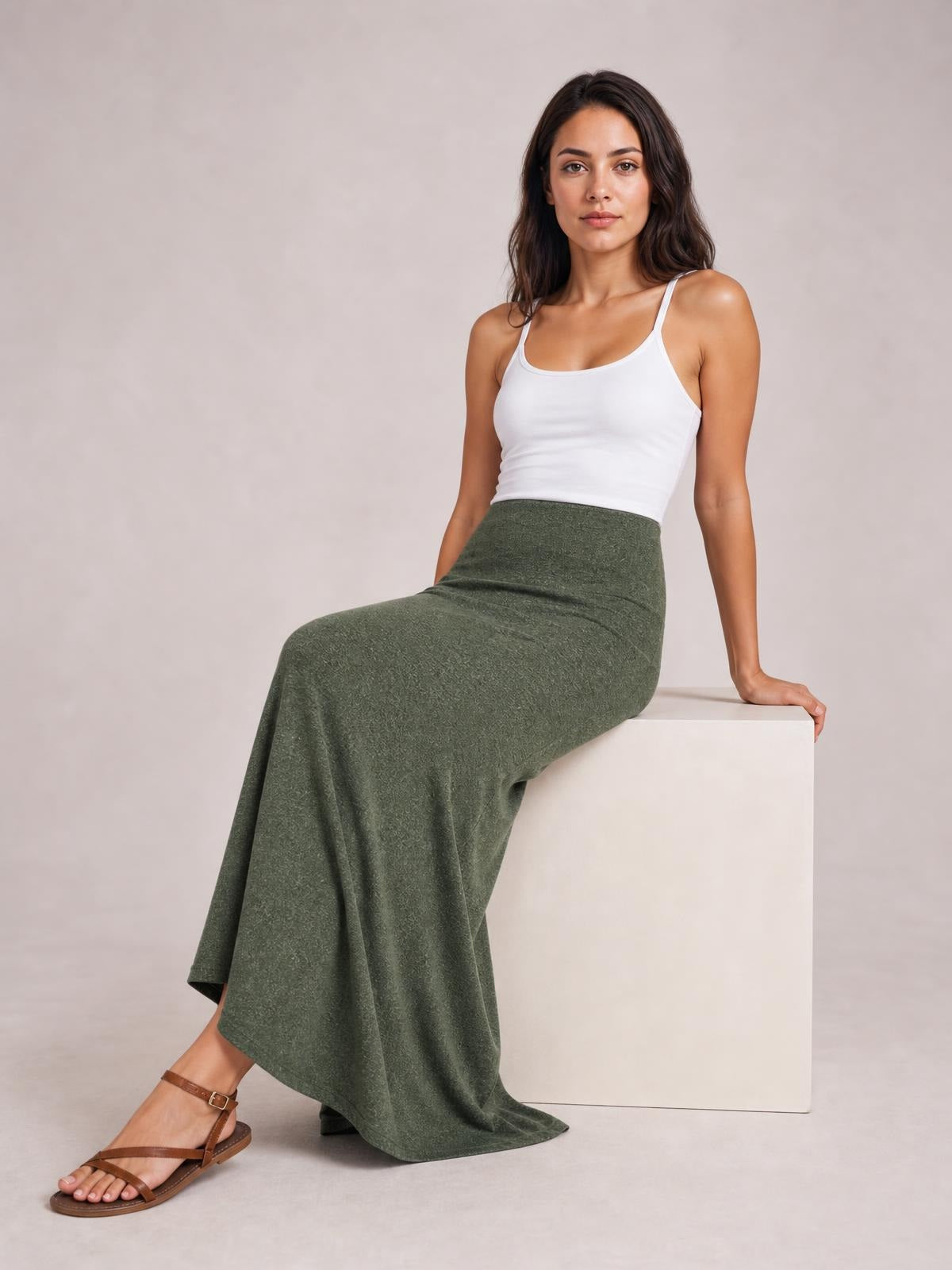Model seated in a relaxed pose wearing a solid olive-green elastic waist maxi skirt with a high-rise fit and flowing floor-length silhouette.