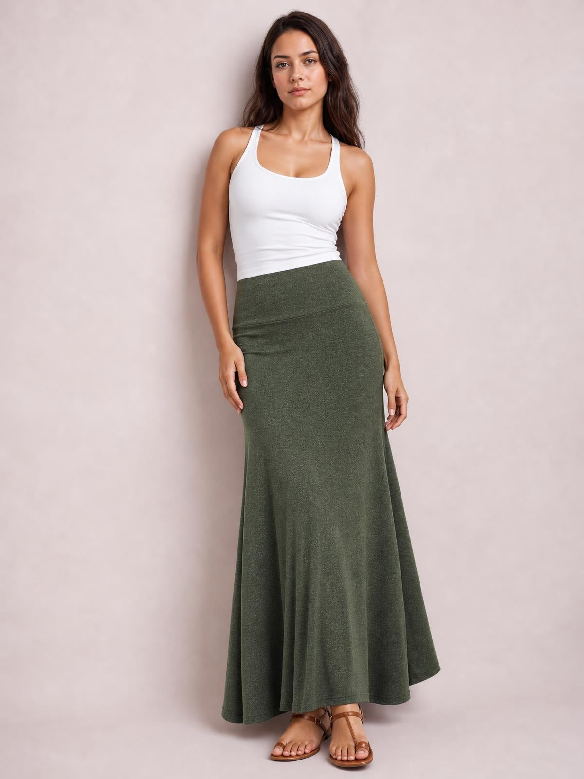 Model poses in a white tank top wearing a solid olive green elastic-waist maxi skirt with a fitted high waist and flowing A-line silhouette.