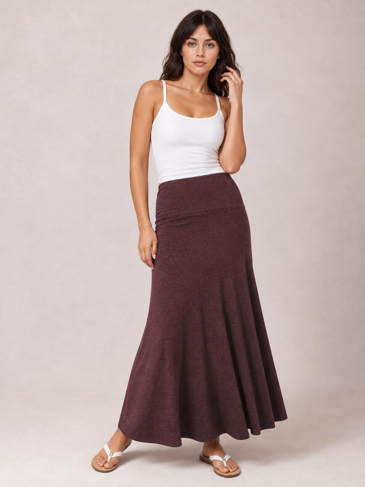 Model poses in a solid burgundy elastic-waist maxi skirt with a fitted upper silhouette and flowy, gently flared hem.