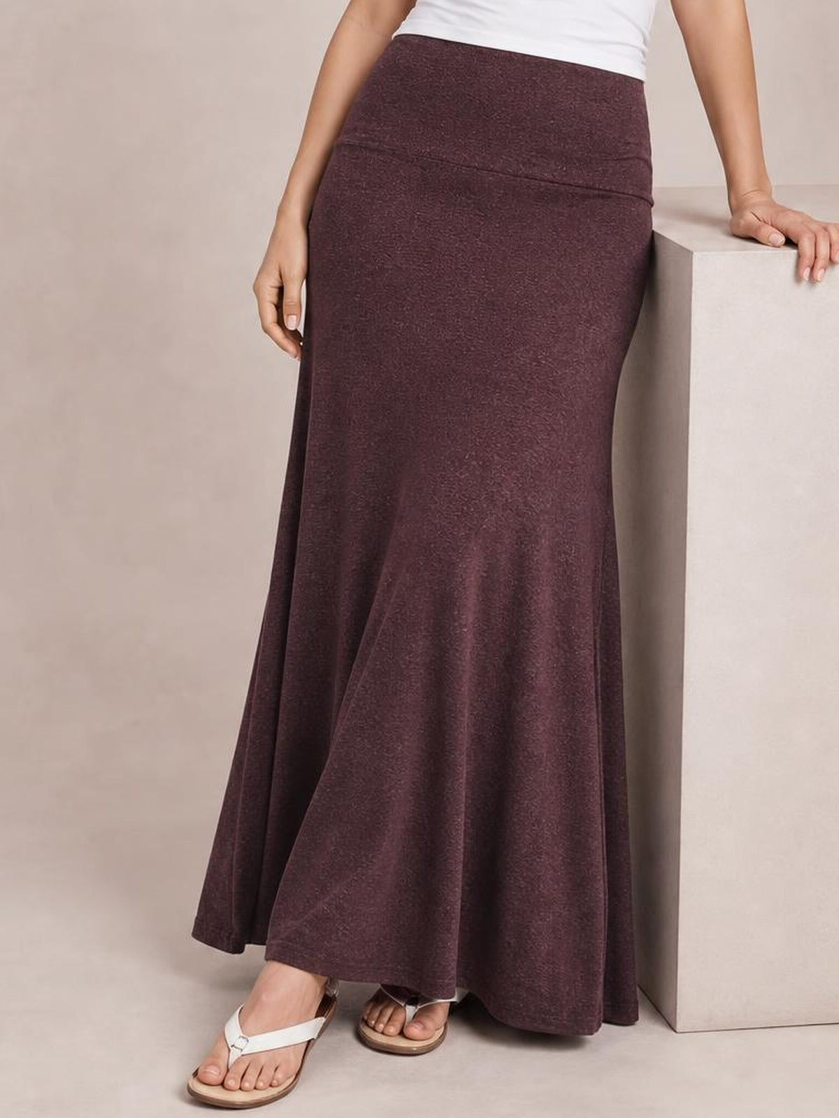 Model wears a solid burgundy elastic-waist maxi skirt with a fitted high-rise silhouette that flows into a softly flared floor-length hem.