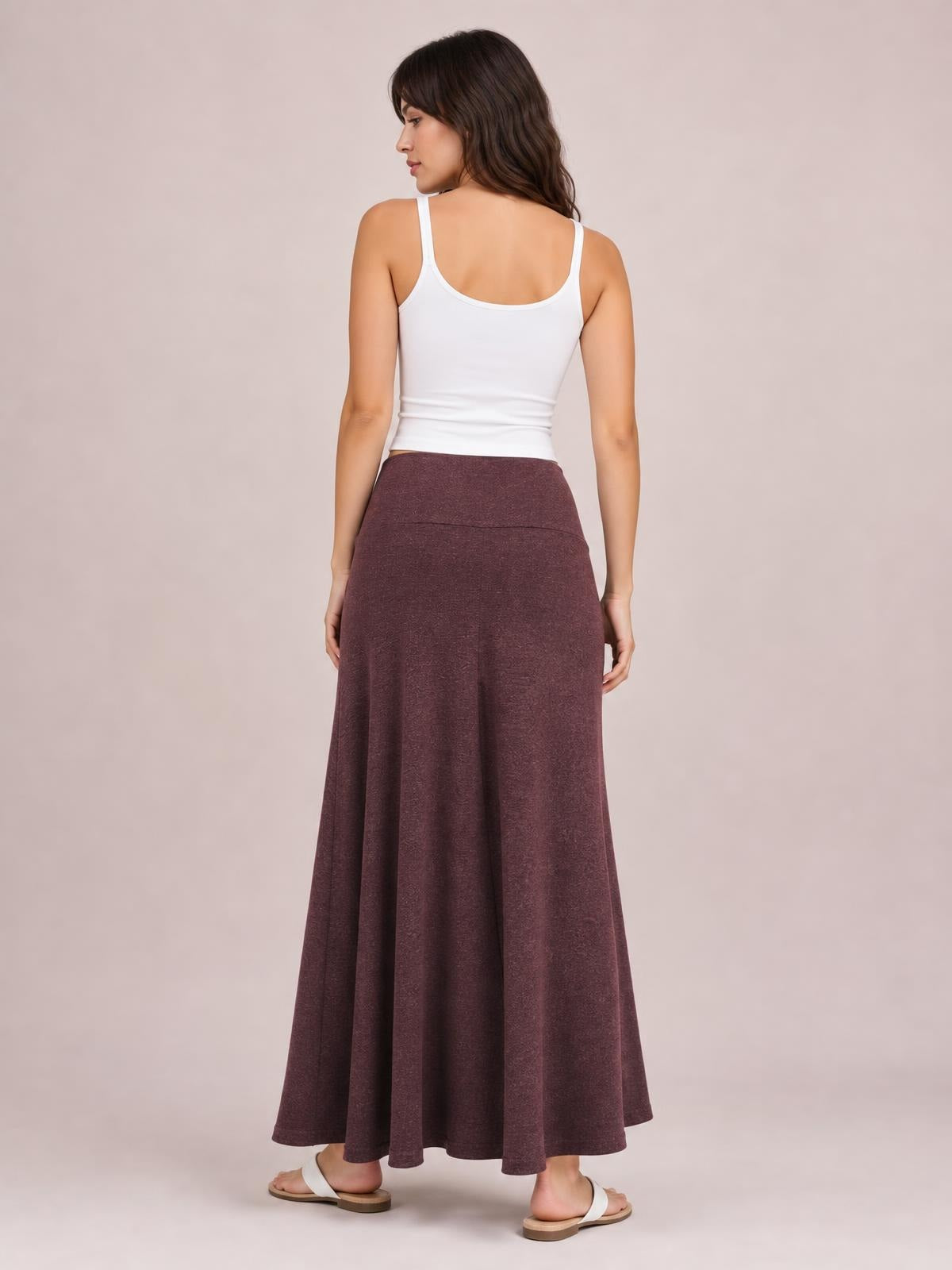 Model seen from behind wearing a solid burgundy elastic-waist maxi skirt with a high-rise fit, flowing A-line silhouette, and smooth waistband.