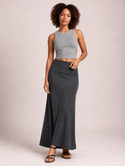 A model stands in black sandals wearing a solid charcoal elastic-waist maxi skirt with a sleek, fitted silhouette that flows gently to the floor.