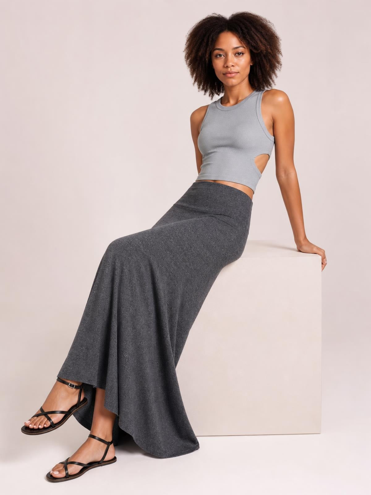 A model sits in a dark gray solid elastic waist maxi skirt with a long, flowy silhouette, smooth waistband, and softly draped construction.
