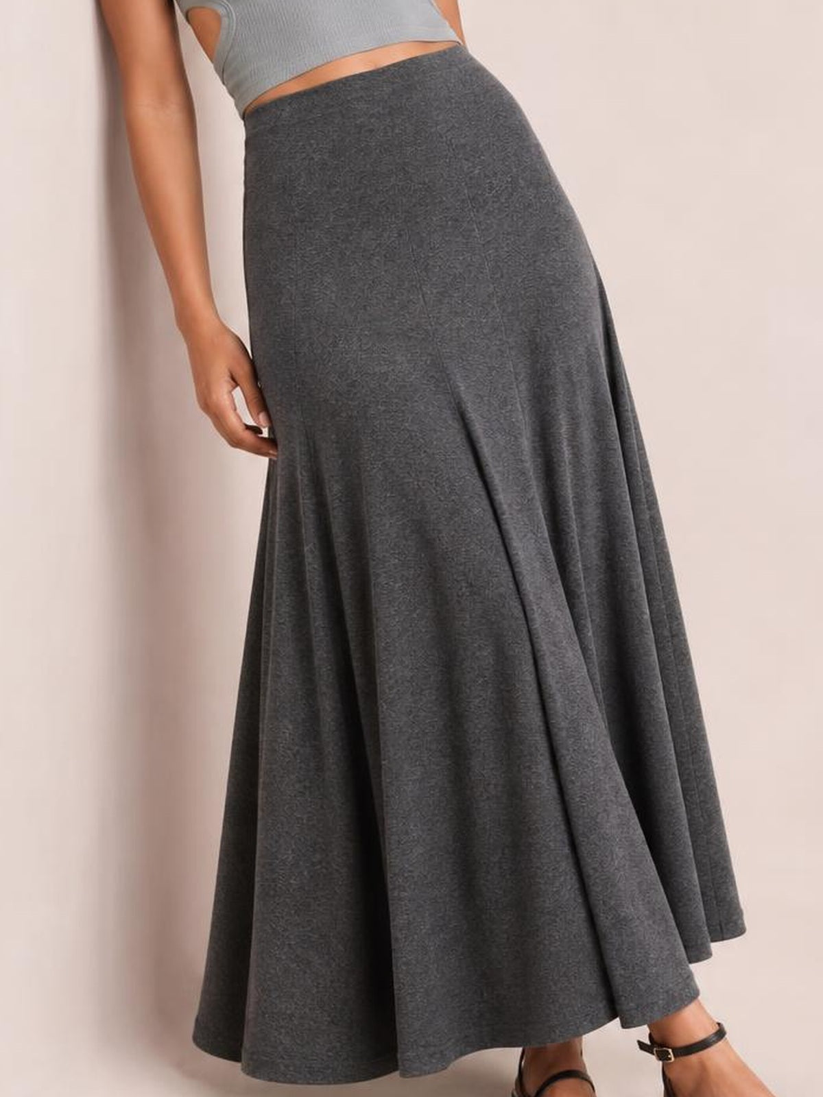 A model poses with one hand touching a solid charcoal-gray elastic-waist maxi skirt featuring a high-rise fit and softly flared, flowy silhouette.