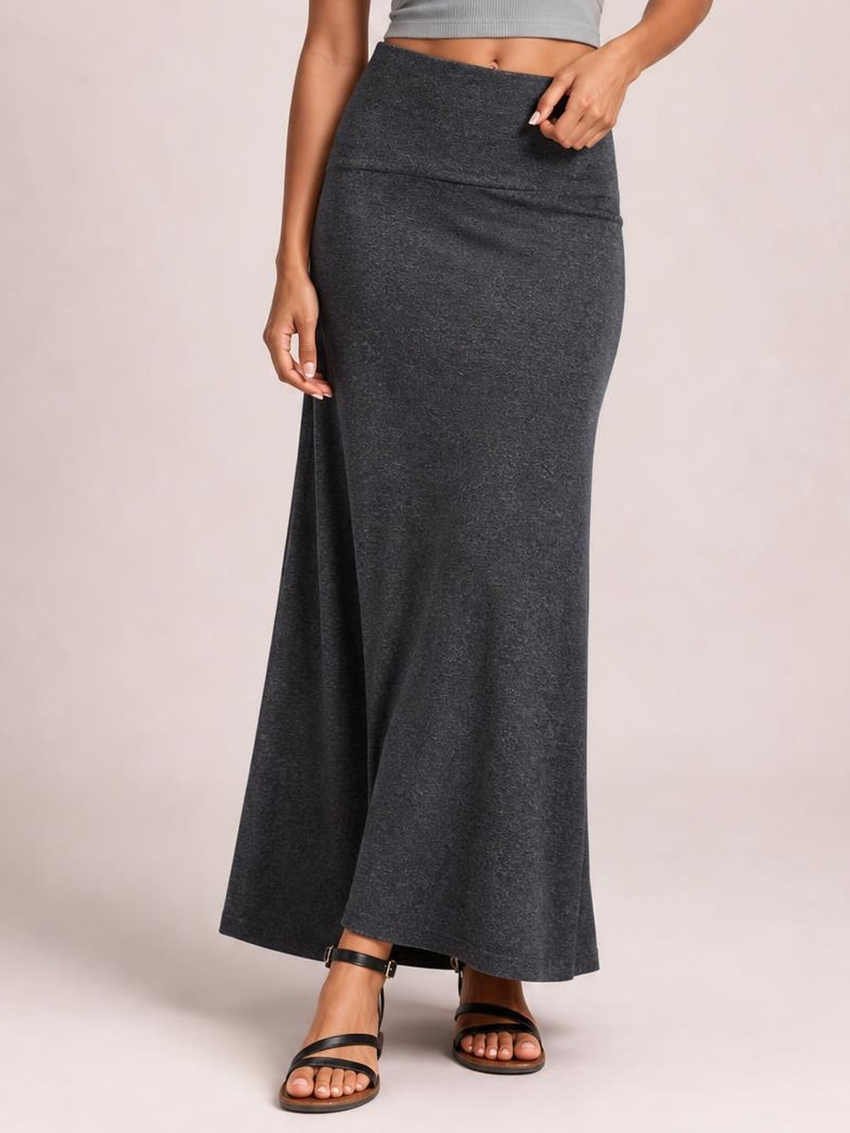 Model poses in a dark gray solid elastic waist maxi skirt with a high waist, smooth fitted silhouette, subtle seam, and gently flared floor-length hem.