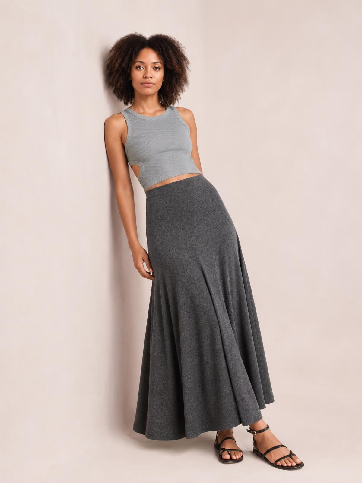 Model poses in a gray solid elastic waist maxi skirt with a fitted waistband and long, flowy silhouette that drapes to the ankles.
