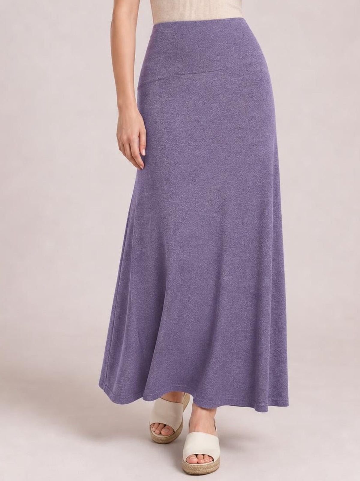 Model wears a solid purple elastic-waist maxi skirt with a high waist, smooth construction, and flowy A-line silhouette, standing with one hand at her side.