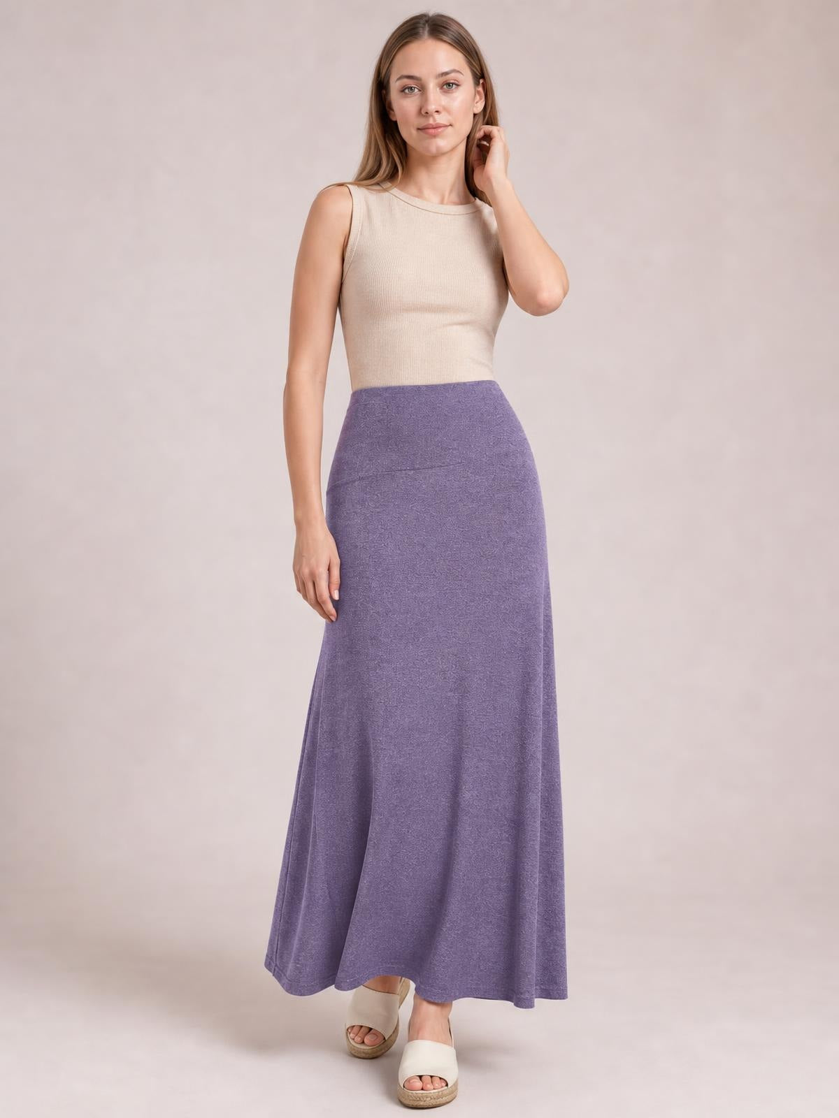 Model poses in a lavender solid elastic waist maxi skirt with a high-rise, close-fitting silhouette that flows into a gently flared hem.
