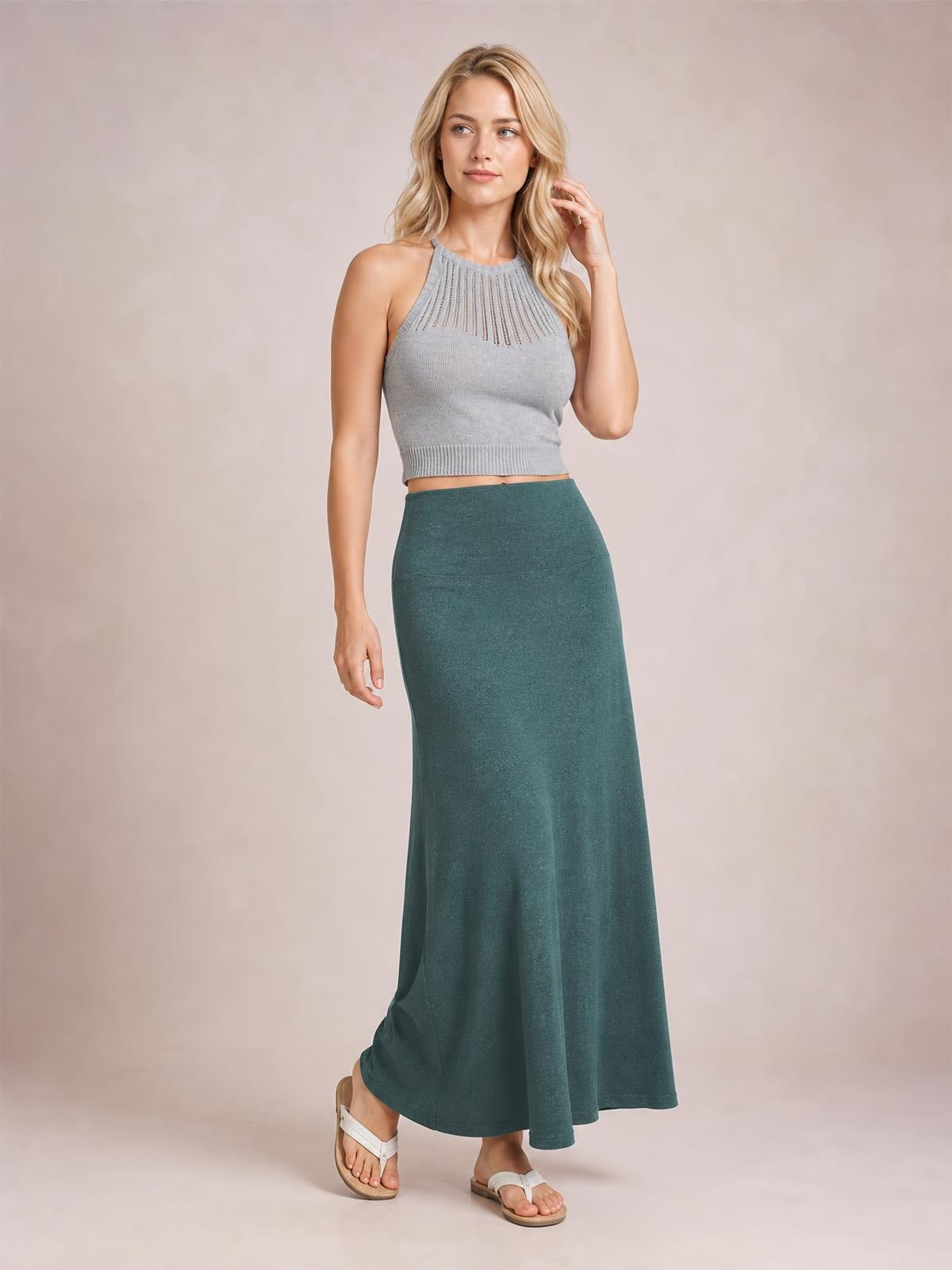 A model poses in a solid deep teal maxi skirt with an elastic waist, fitted hip, and softly flared, flowy silhouette.