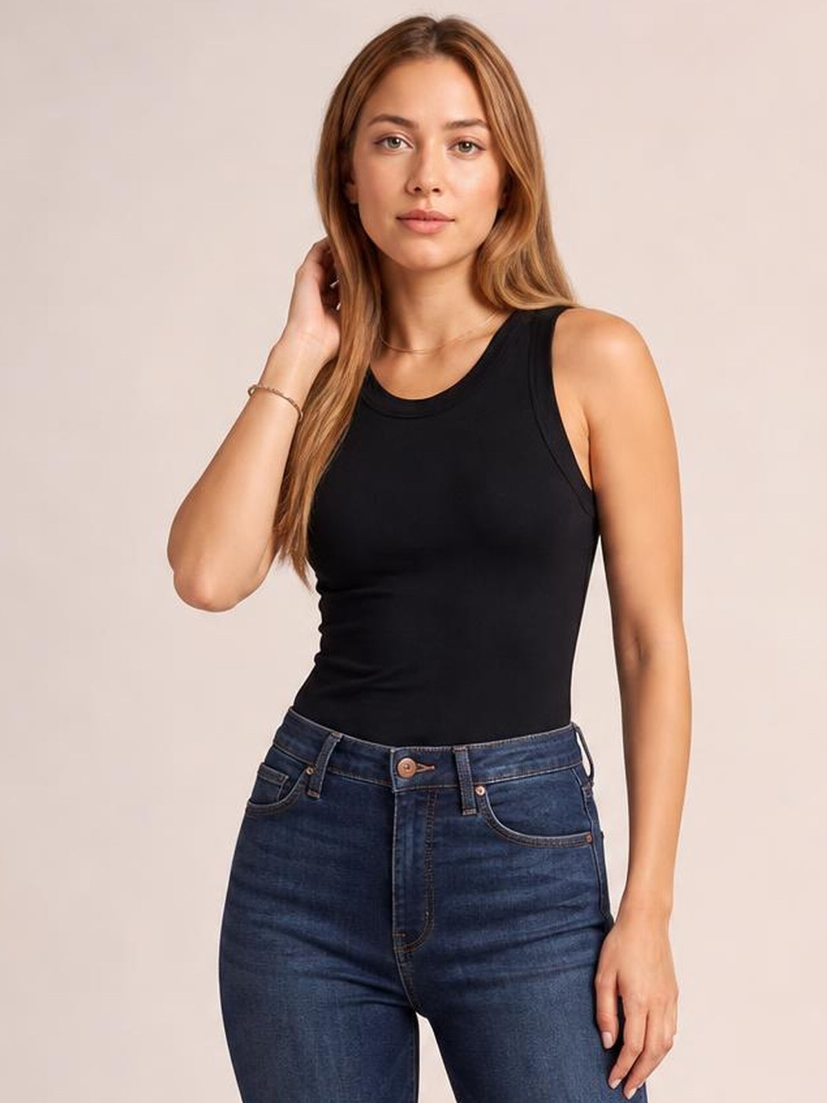 Model poses in a black solid round neck tank with wide shoulder straps, a fitted silhouette, and slight stretch for a smooth everyday look.