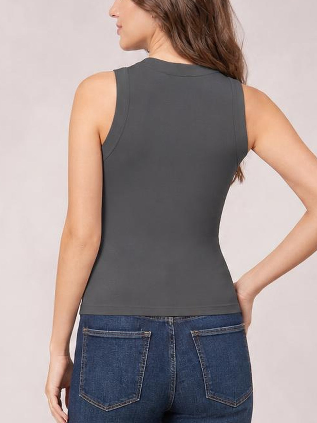 Back view of a model wearing a solid charcoal round neck tank with sleeveless styling, a fitted silhouette, clean armholes, and a straight hem.