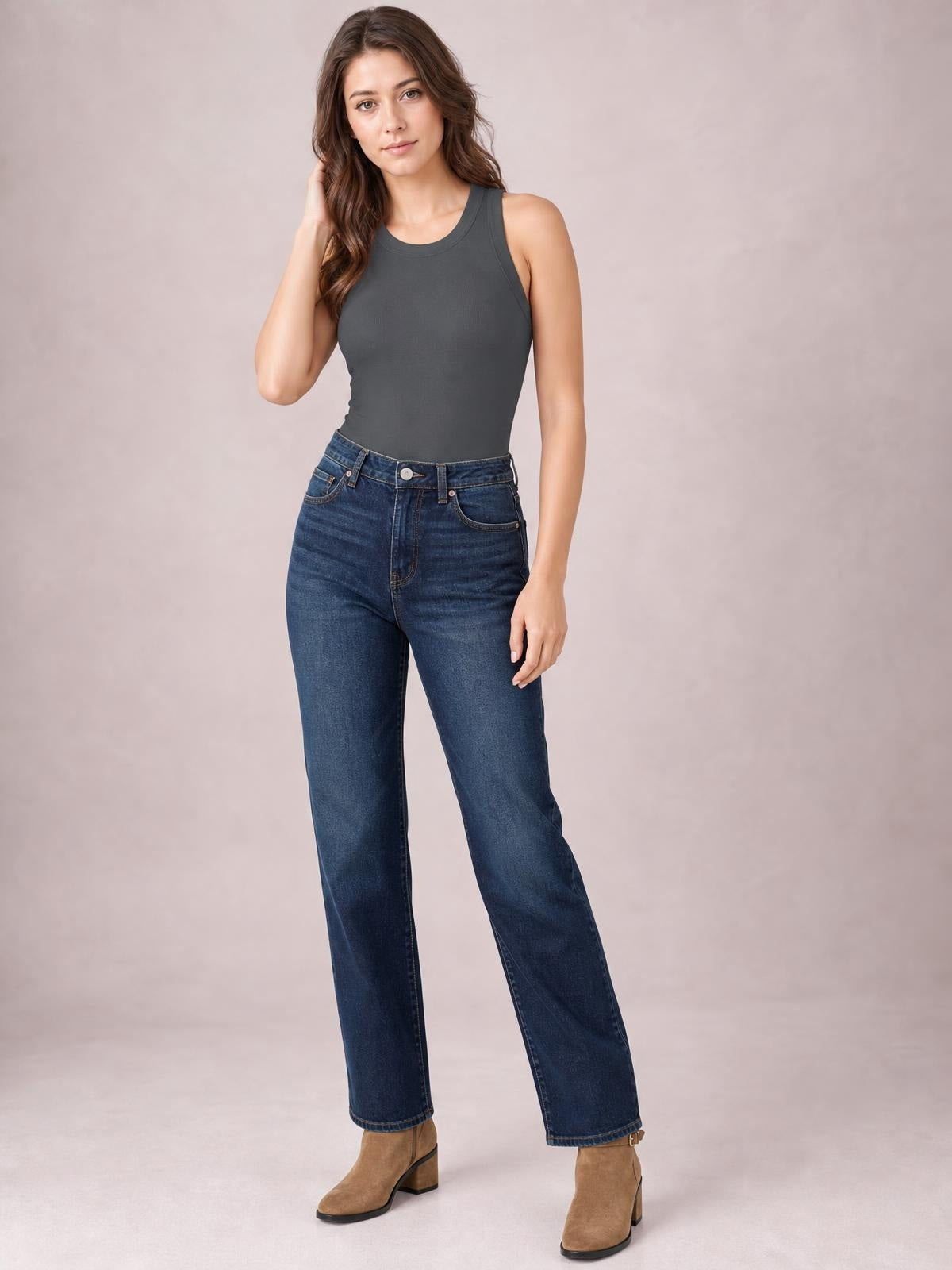Model poses in a charcoal solid round neck tank with wide shoulder straps, a fitted silhouette, and subtle stretch, paired with jeans.