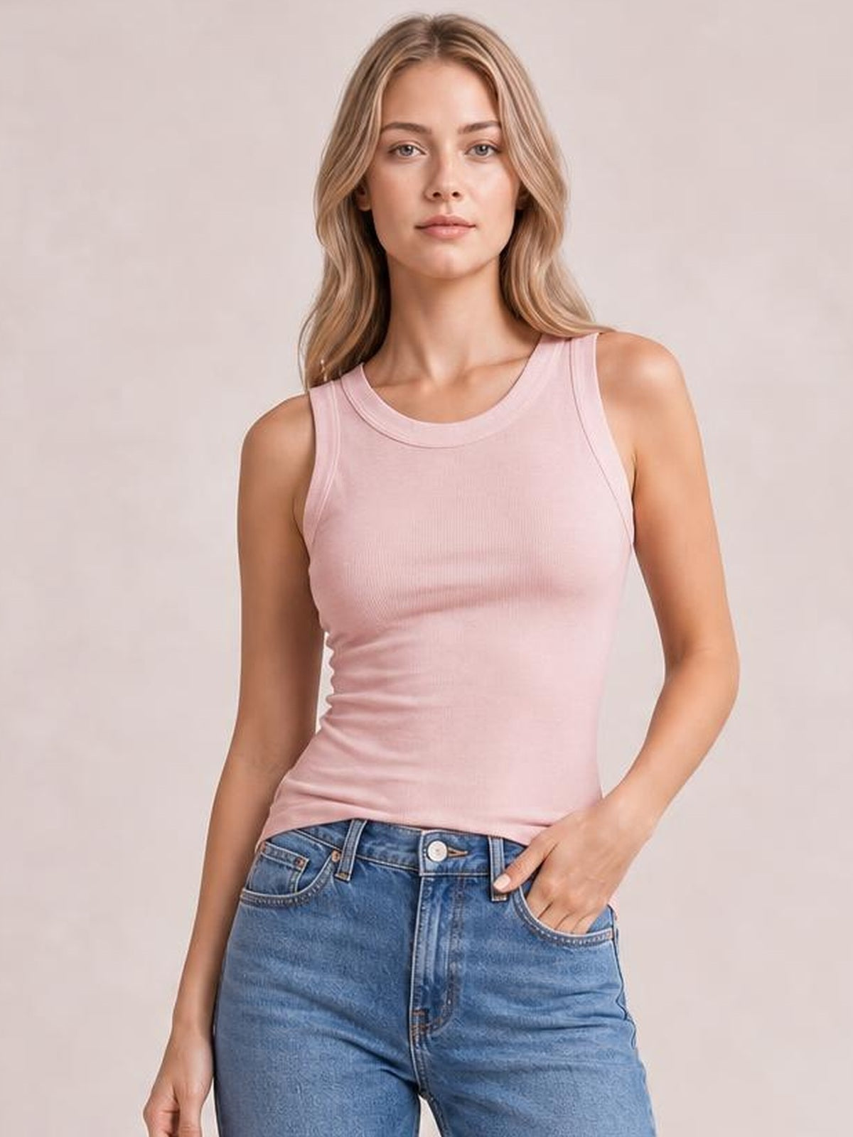 Model wearing a solid pink round neck tank with wide shoulder straps and a fitted, slightly stretchy silhouette, paired with blue jeans.