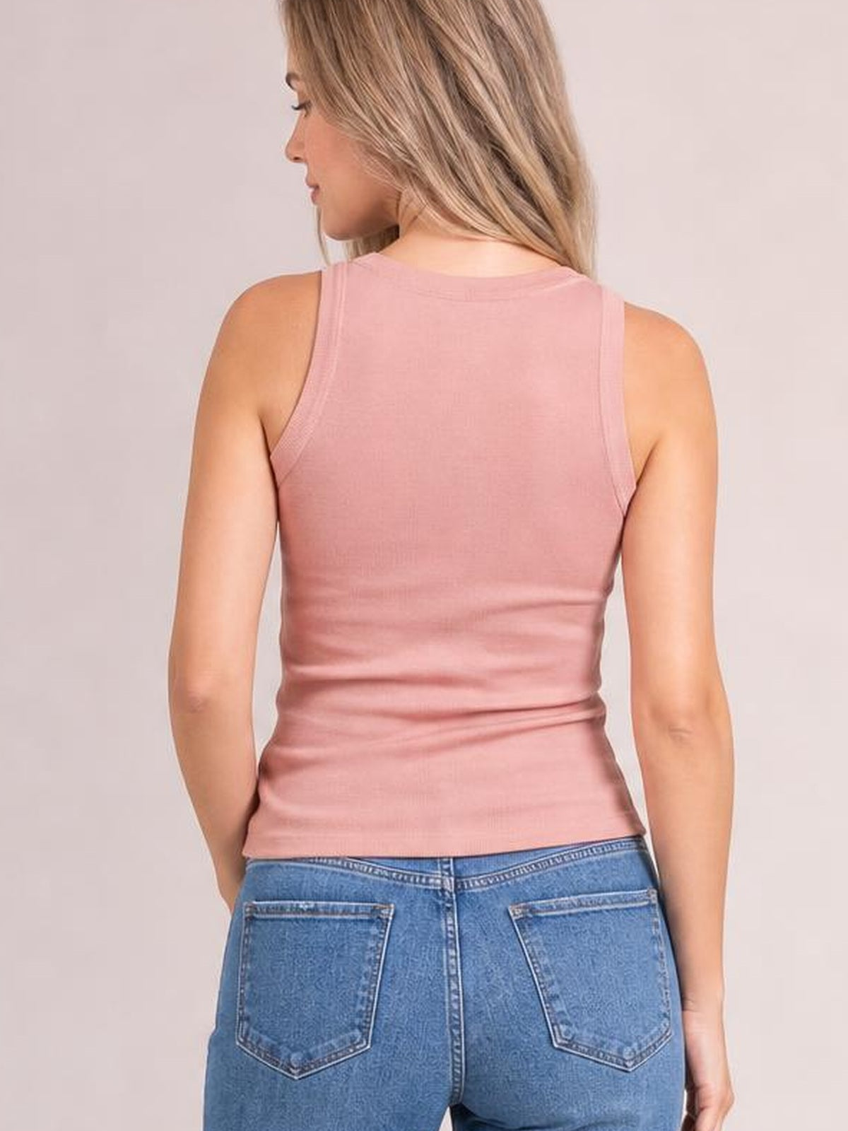 Model turned away wears a solid pink round neck tank with wide shoulder straps, a fitted silhouette, and clean, simple construction.