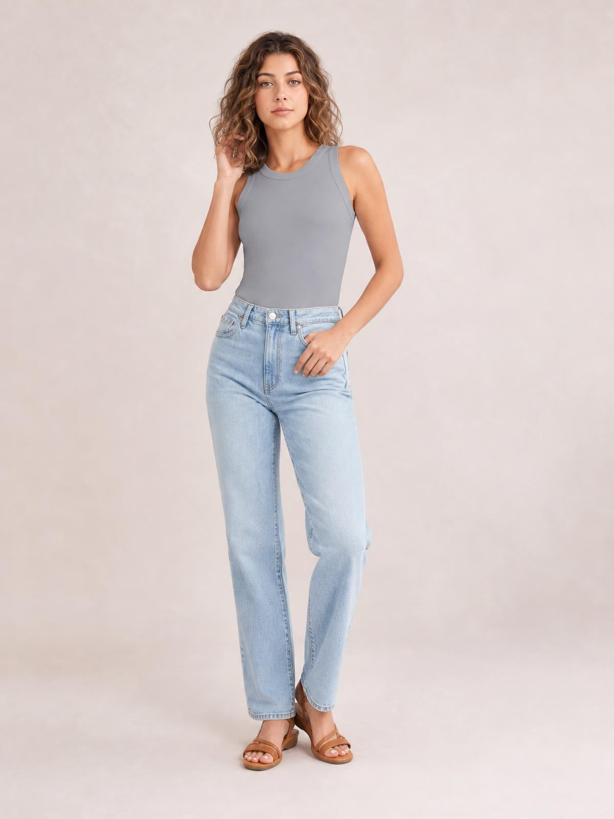 Model poses in a solid gray round neck tank with wide shoulder straps and a fitted silhouette, styled with light-wash jeans.