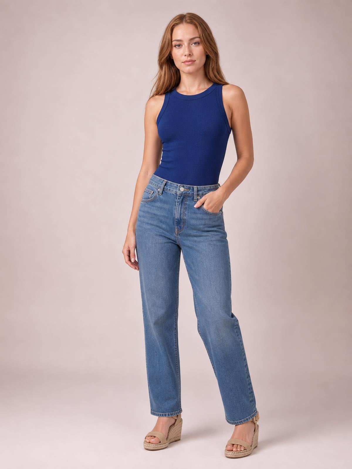 Model wearing a solid navy round neck tank with wide shoulder straps, sleeveless cut, and a fitted silhouette, posed with one hand in her jeans pocket.