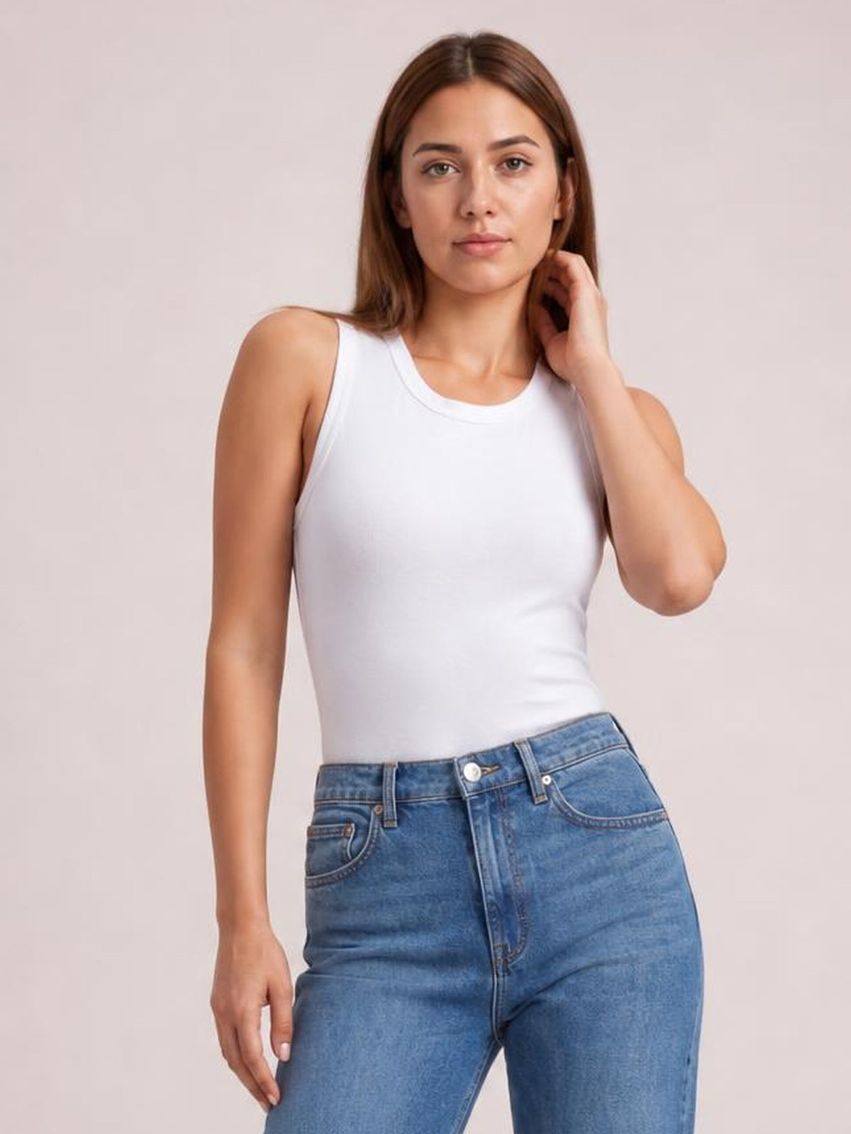 Model wearing a solid white round neck tank with slim shoulder straps and a fitted silhouette, posing with one hand touching her hair.