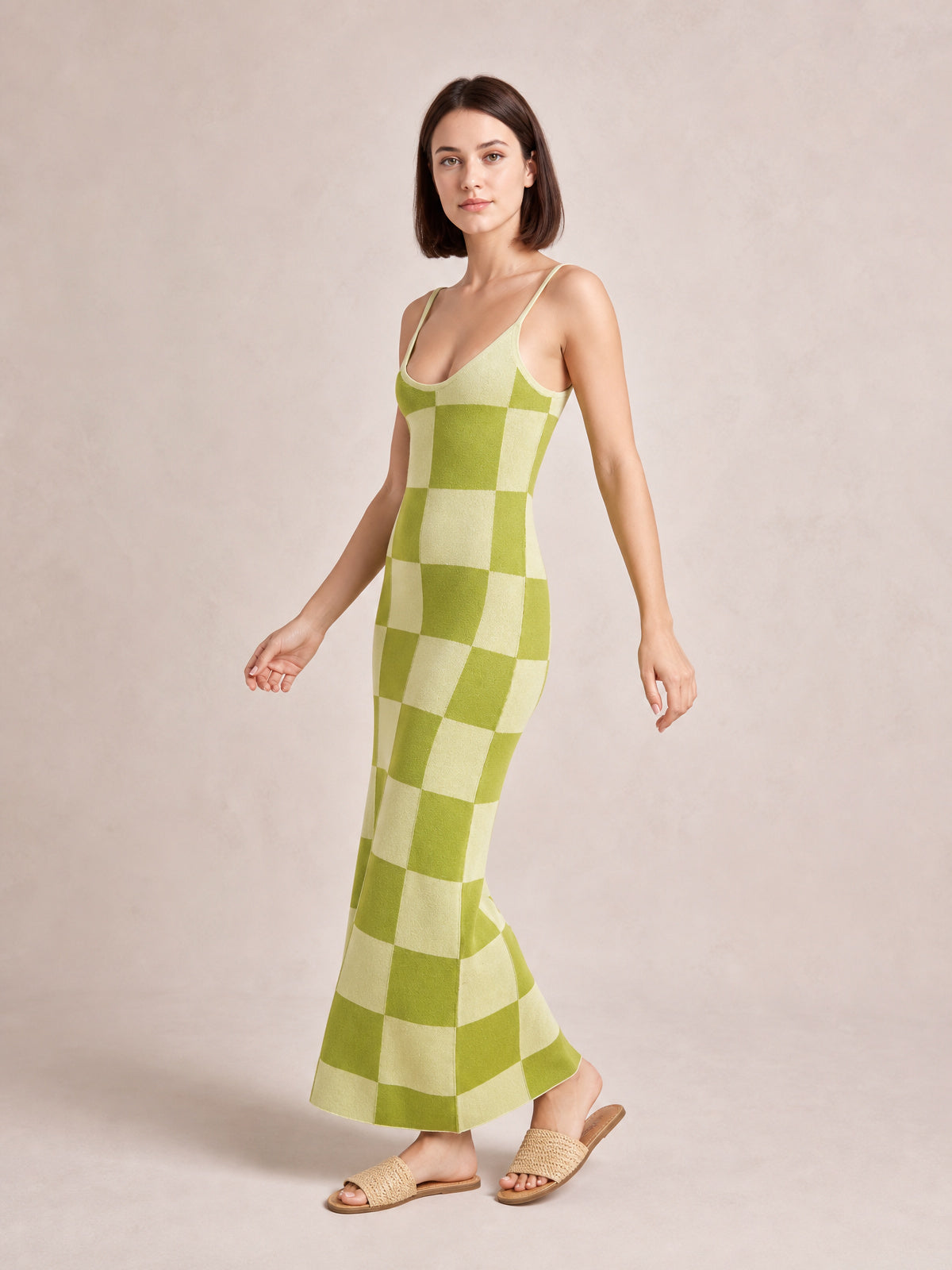 Model poses in a green and cream checkerboard spaghetti strap maxi sweater dress with a scoop neckline, fitted silhouette, and gently flared ankle-length hem.