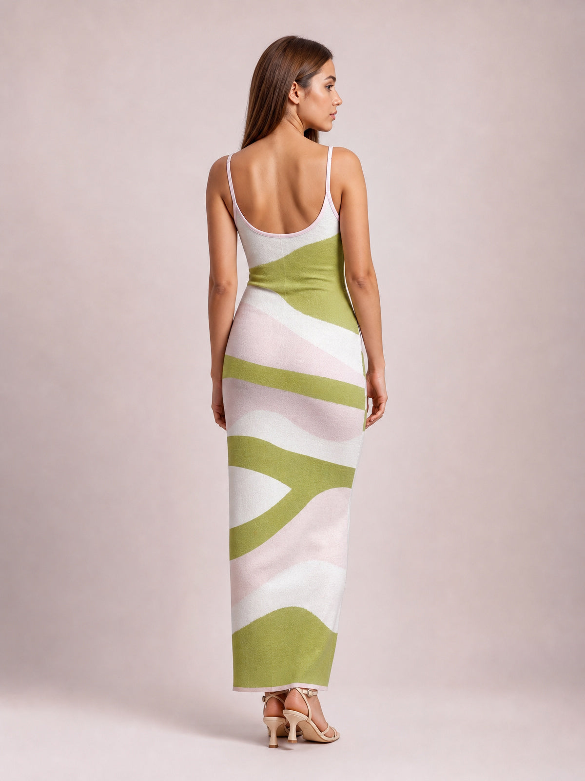 Model shown from behind in a fitted spaghetti strap maxi sweater dress with a scoop back and abstract green, pink, and white pattern.