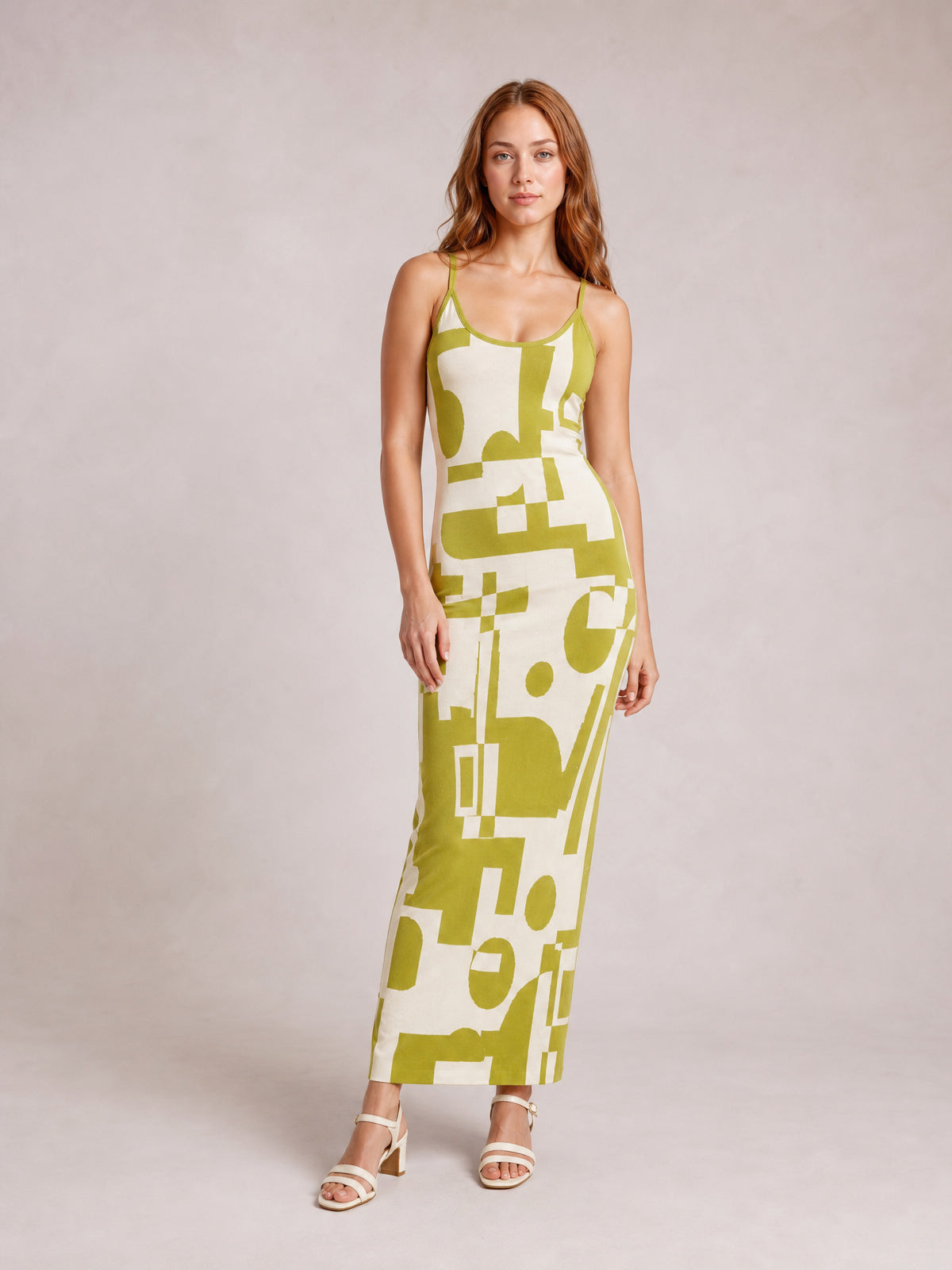 A model stands in a fitted spaghetti strap maxi sweater dress with a scoop neckline, olive green and cream geometric print, and an ankle-skimming silhouette.