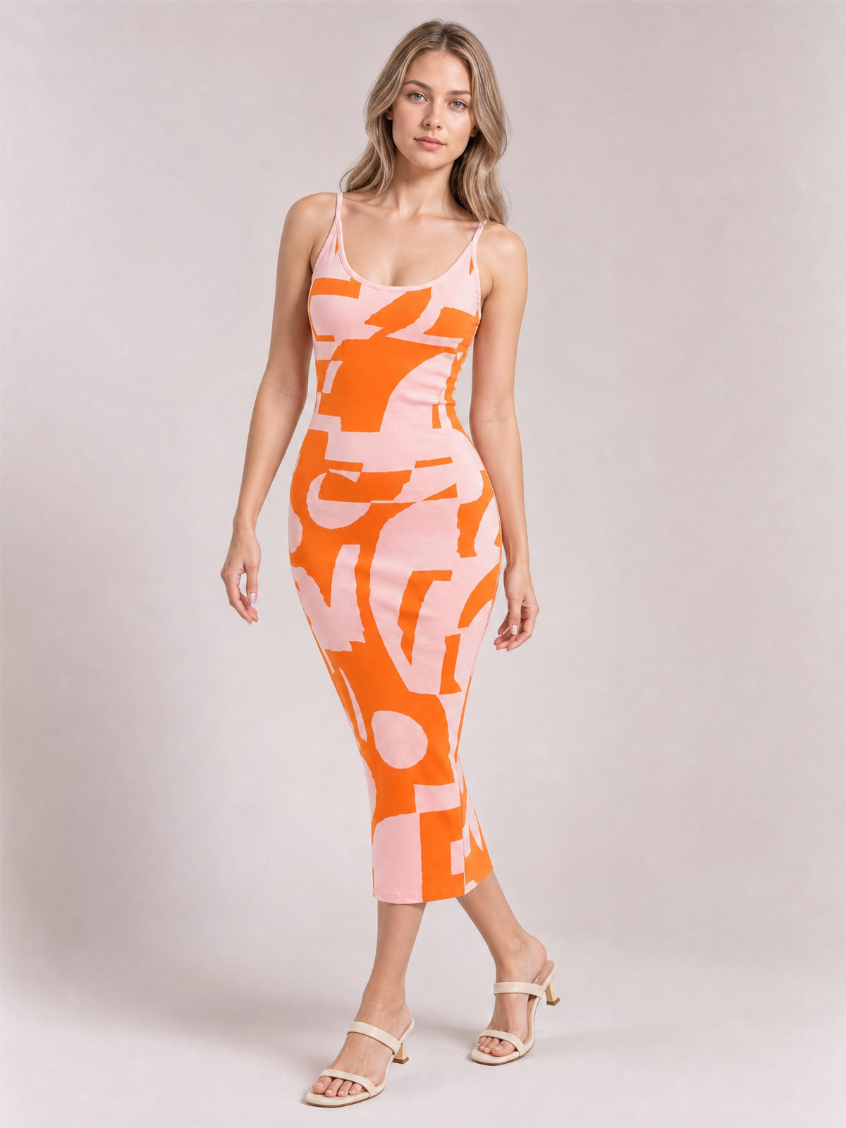 Model poses in a pink and orange abstract-print spaghetti strap sweater dress with an open neckline, fitted midi silhouette, and stretchy construction.