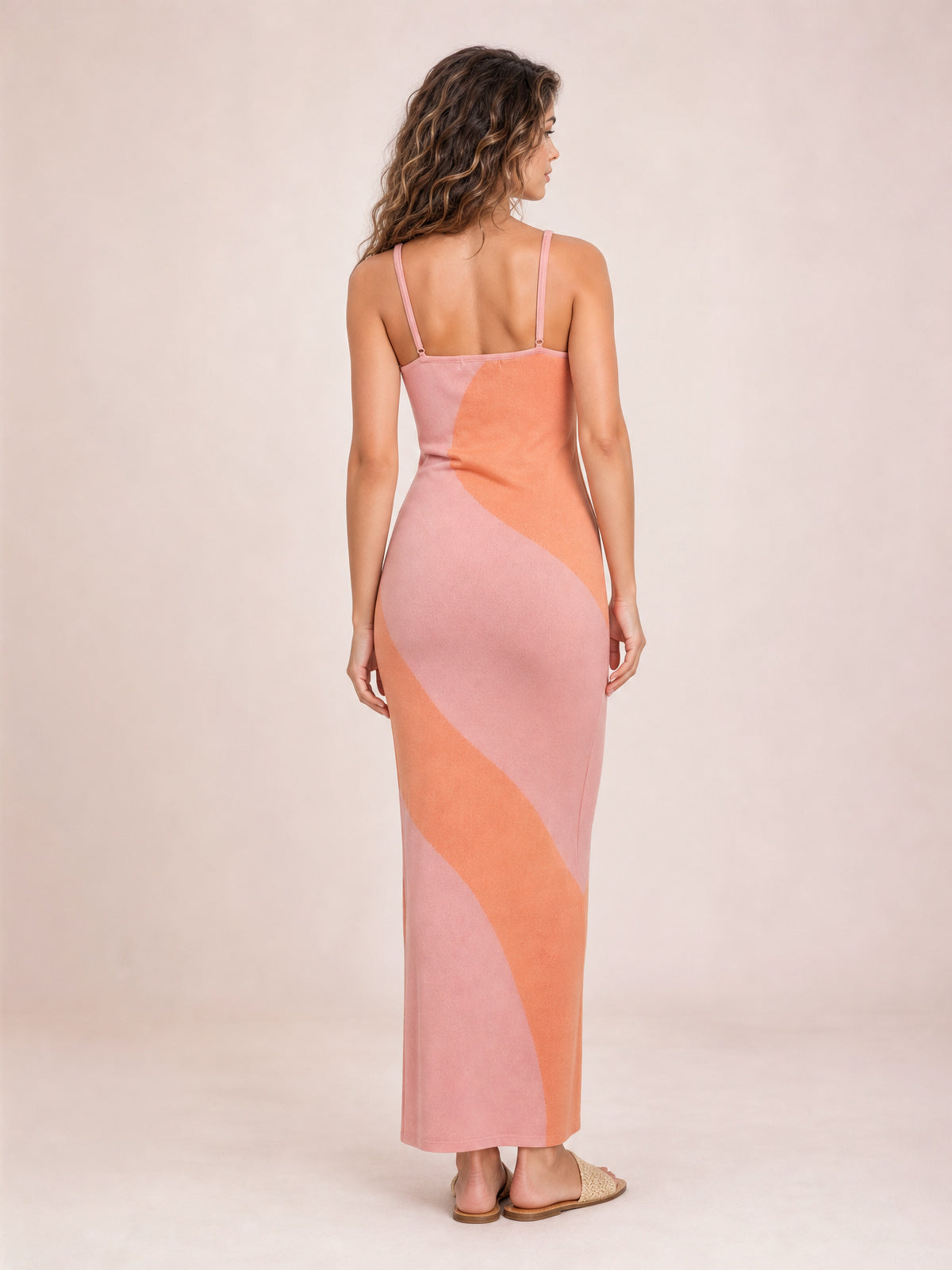 Back view of a model in a pink and orange spaghetti strap maxi sweater dress with a fitted silhouette, straight neckline, and ankle-skimming hem.