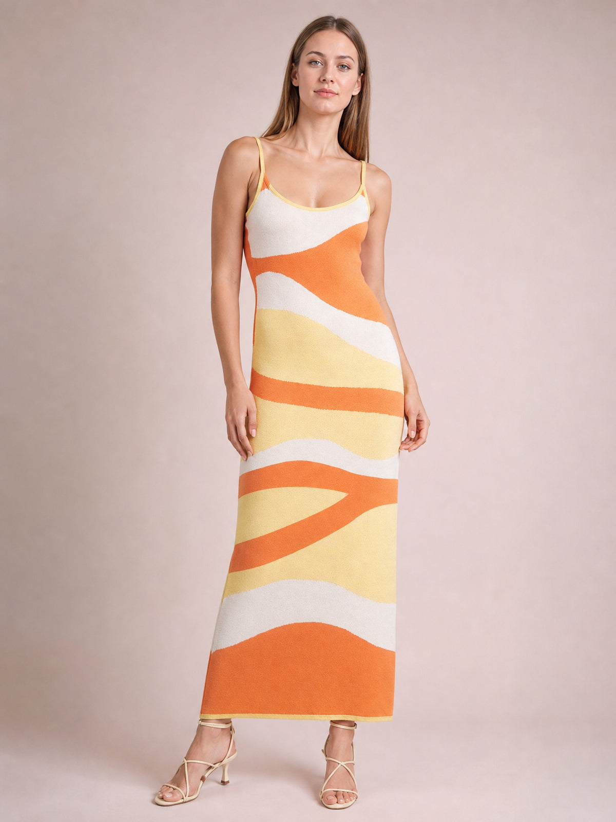 Model wears a spaghetti strap maxi sweater dress with a fitted silhouette, scoop neckline, and bold orange, cream, and yellow wave stripes.