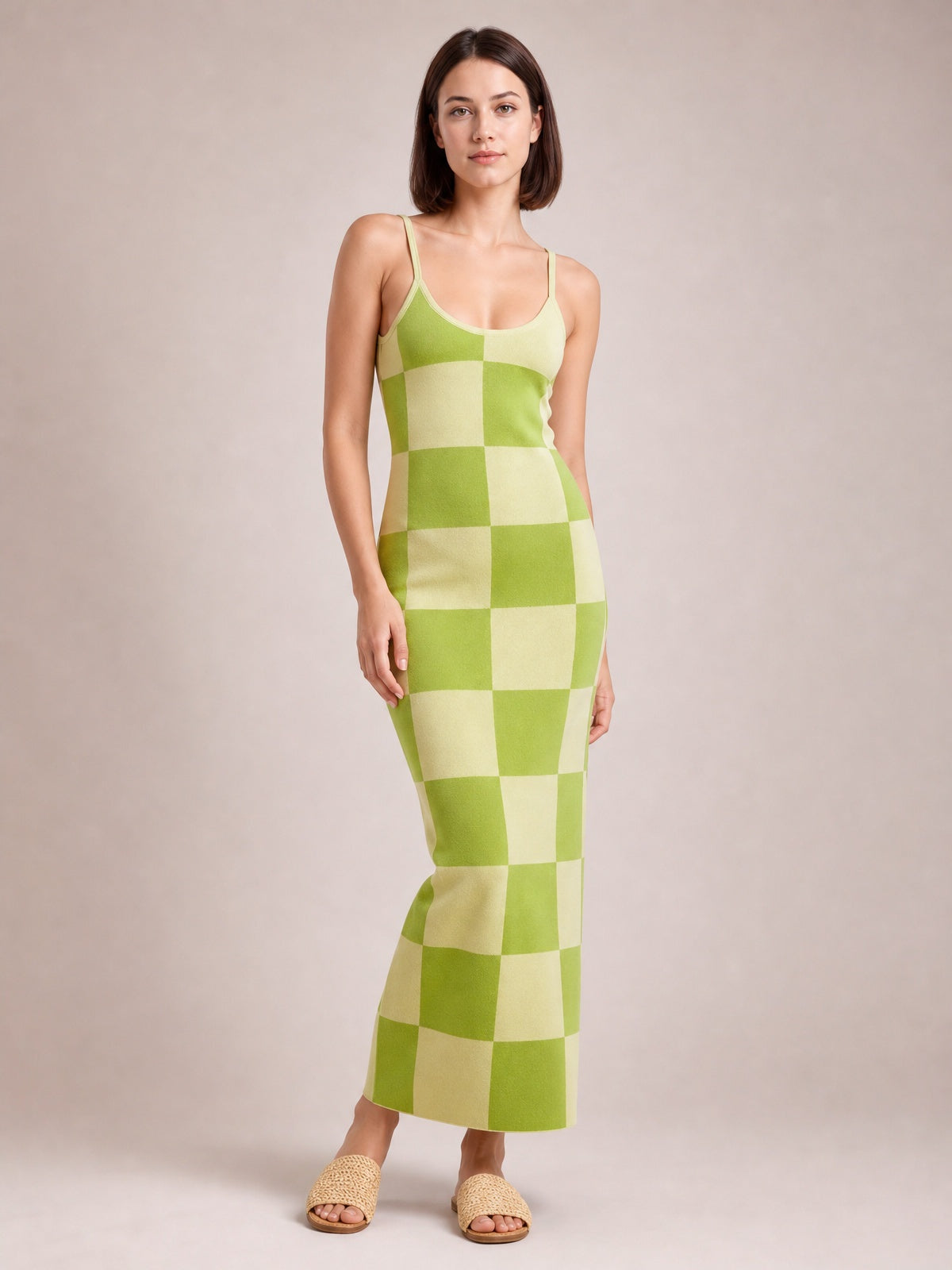 A model stands in a green and pale yellow checkerboard spaghetti strap maxi sweater dress with a fitted, stretchy silhouette and ankle-skimming hem.