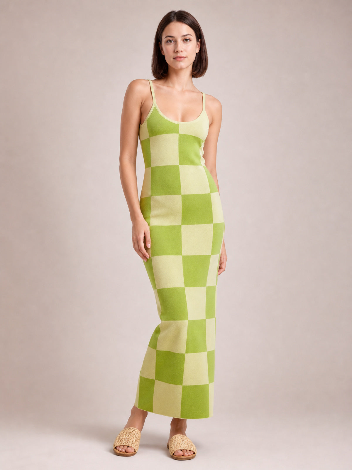 A model stands in a green and pale yellow checkerboard spaghetti strap maxi sweater dress with a fitted, stretchy silhouette and ankle-skimming hem.