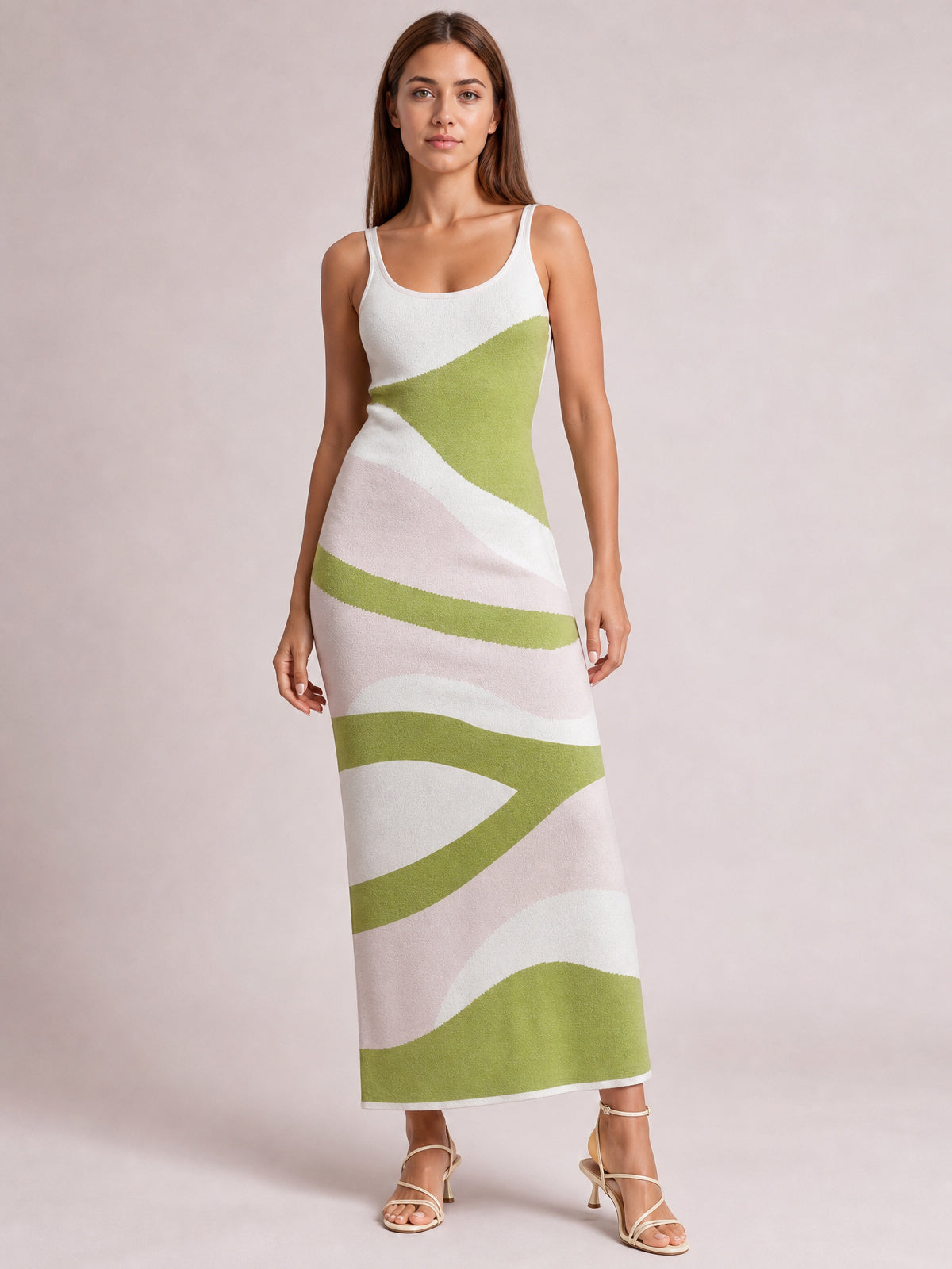 Model stands in a fitted spaghetti-strap maxi sweater dress with a scoop neckline, ankle-skimming silhouette, and abstract green, white, and blush pattern.