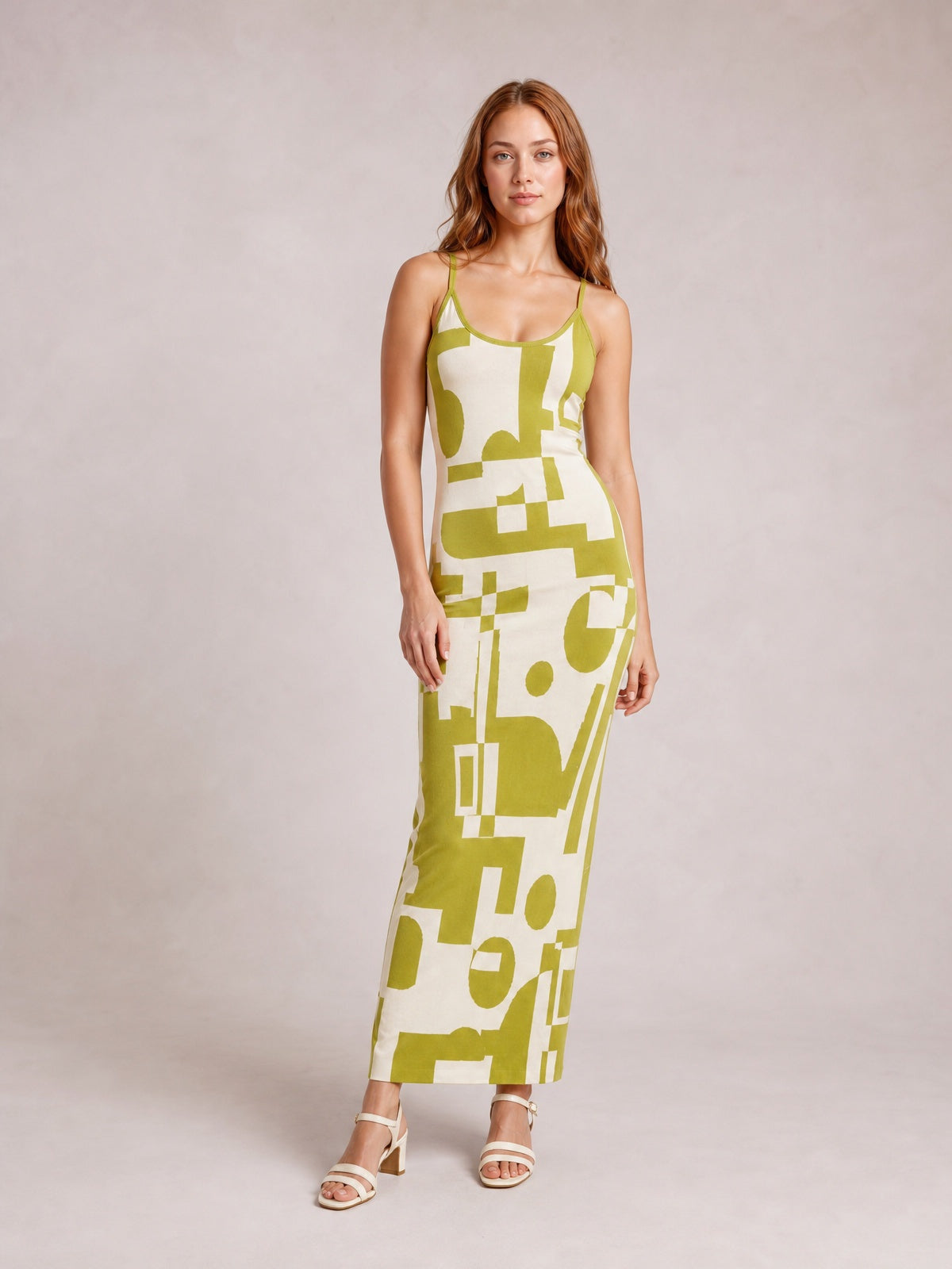 A model stands in a fitted spaghetti strap maxi sweater dress with a scoop neckline, olive green and cream geometric print, and an ankle-skimming silhouette.