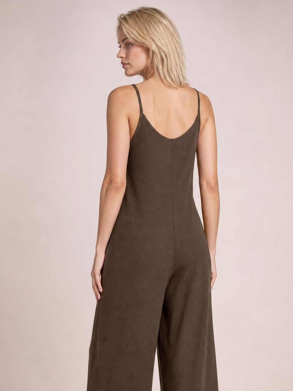 Model shown from behind in a brown spaghetti-strap jumpsuit with a low scoop back, ribbed texture, fitted waist, and flowing wide-leg silhouette.