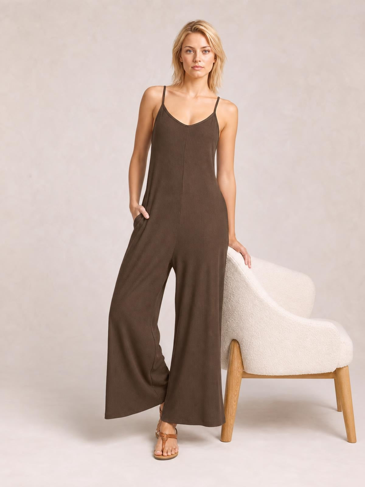 Model poses in a brown spaghetti strap V-neck jumpsuit with a relaxed wide-leg silhouette, ribbed texture, and side pockets.