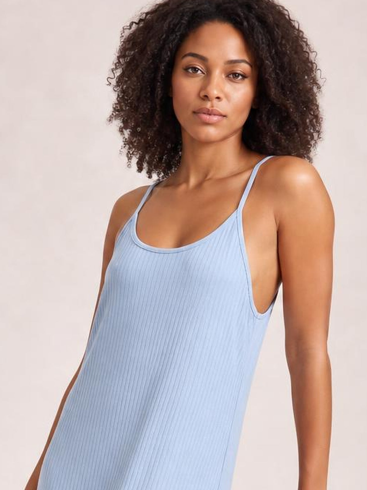 Model faces the camera wearing a light blue spaghetti-strap jumpsuit with a softly scooped neckline, fine ribbed texture, and a relaxed straight silhouette.