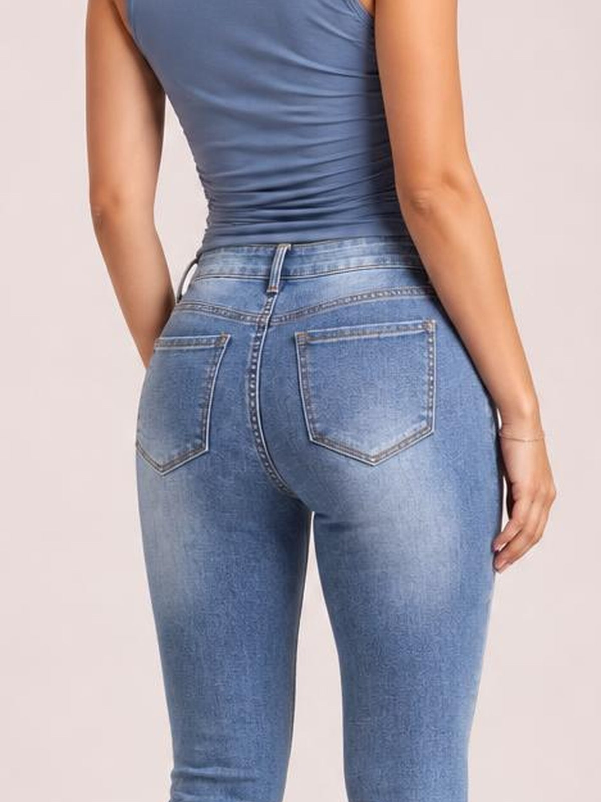 A model poses from behind in light-wash sparkling rhinestone high-waist skinny jeans with a fitted silhouette, belt loops, contrast stitching, and back pockets.