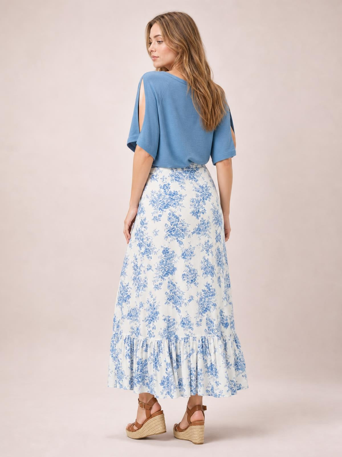 Model shown from behind in a white and blue floral printed skirt with a flowing A-line silhouette, gathered ruffled tier, and ankle-length hem.