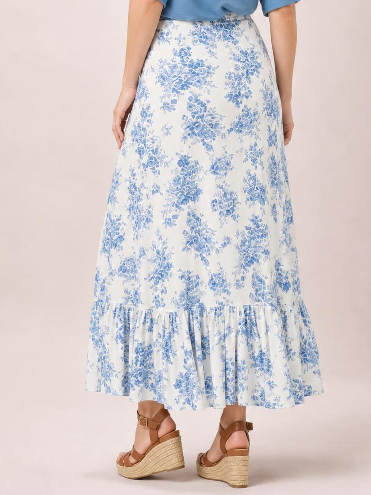 Model wearing a white and blue floral printed skirt with a flowing asymmetrical silhouette and gathered ruffle hem, shown from the back.