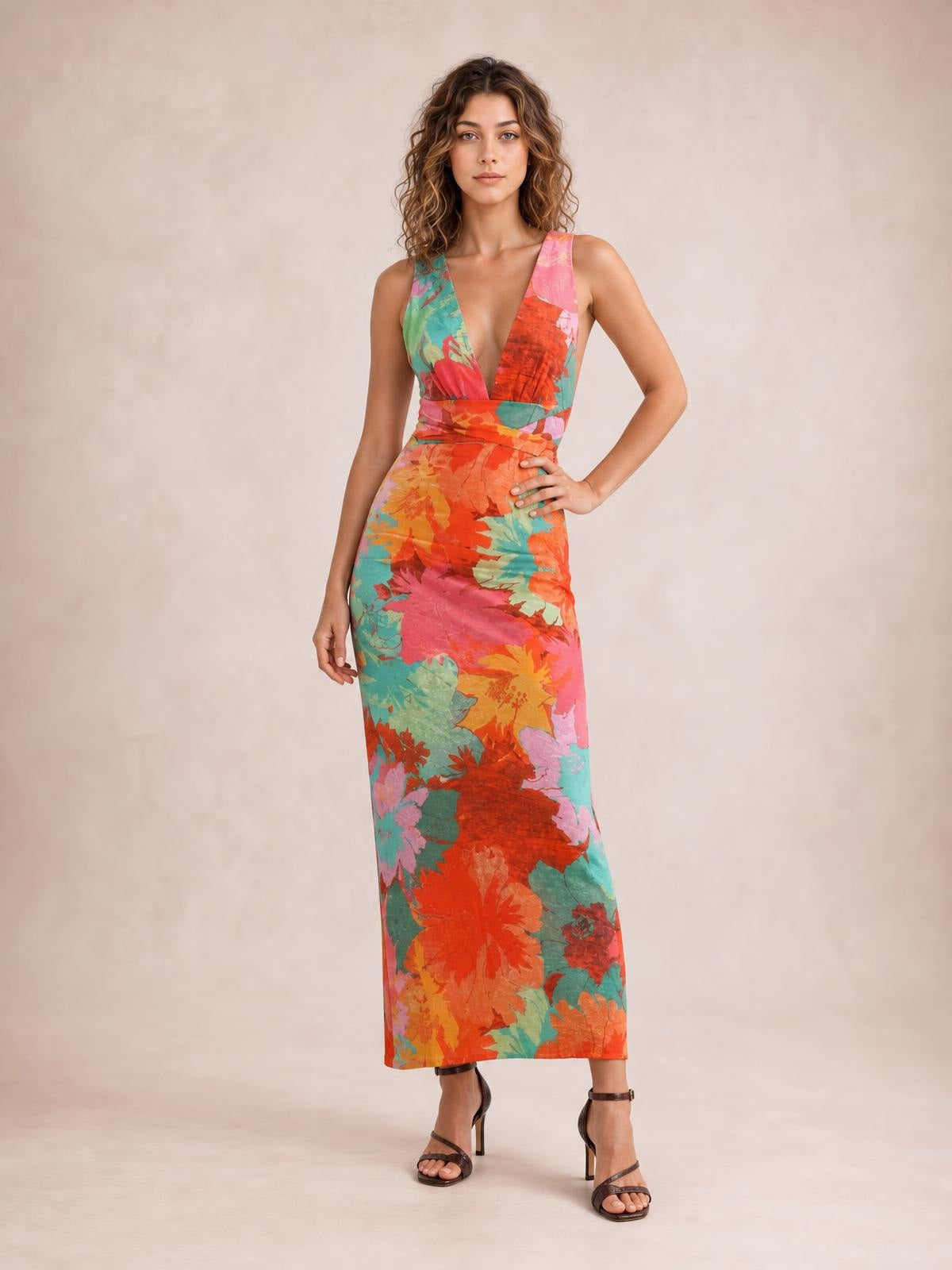 Model poses in a vibrant floral printed plunge maxi dress with tied waist, wide shoulder straps, and a slim, floor-length silhouette.