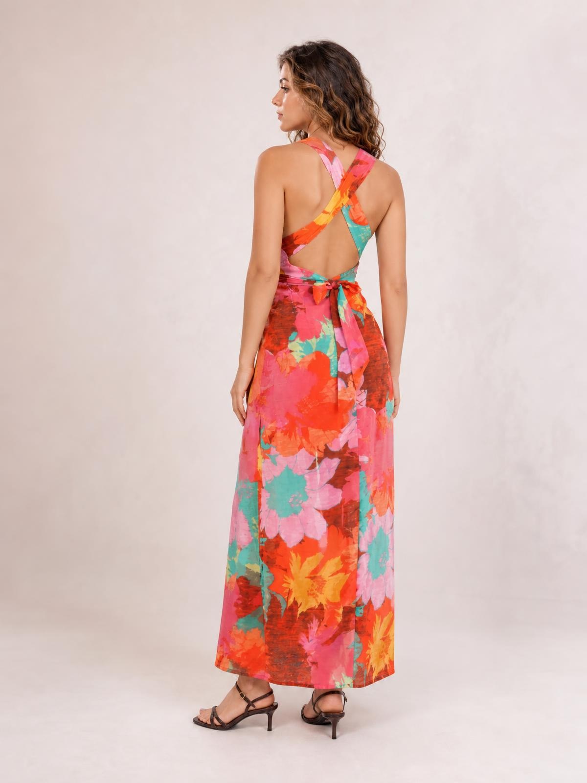 Model turned away in a vibrant floral printed maxi dress with crisscross back straps, an open back, tied waist, and straight floor-length silhouette.
