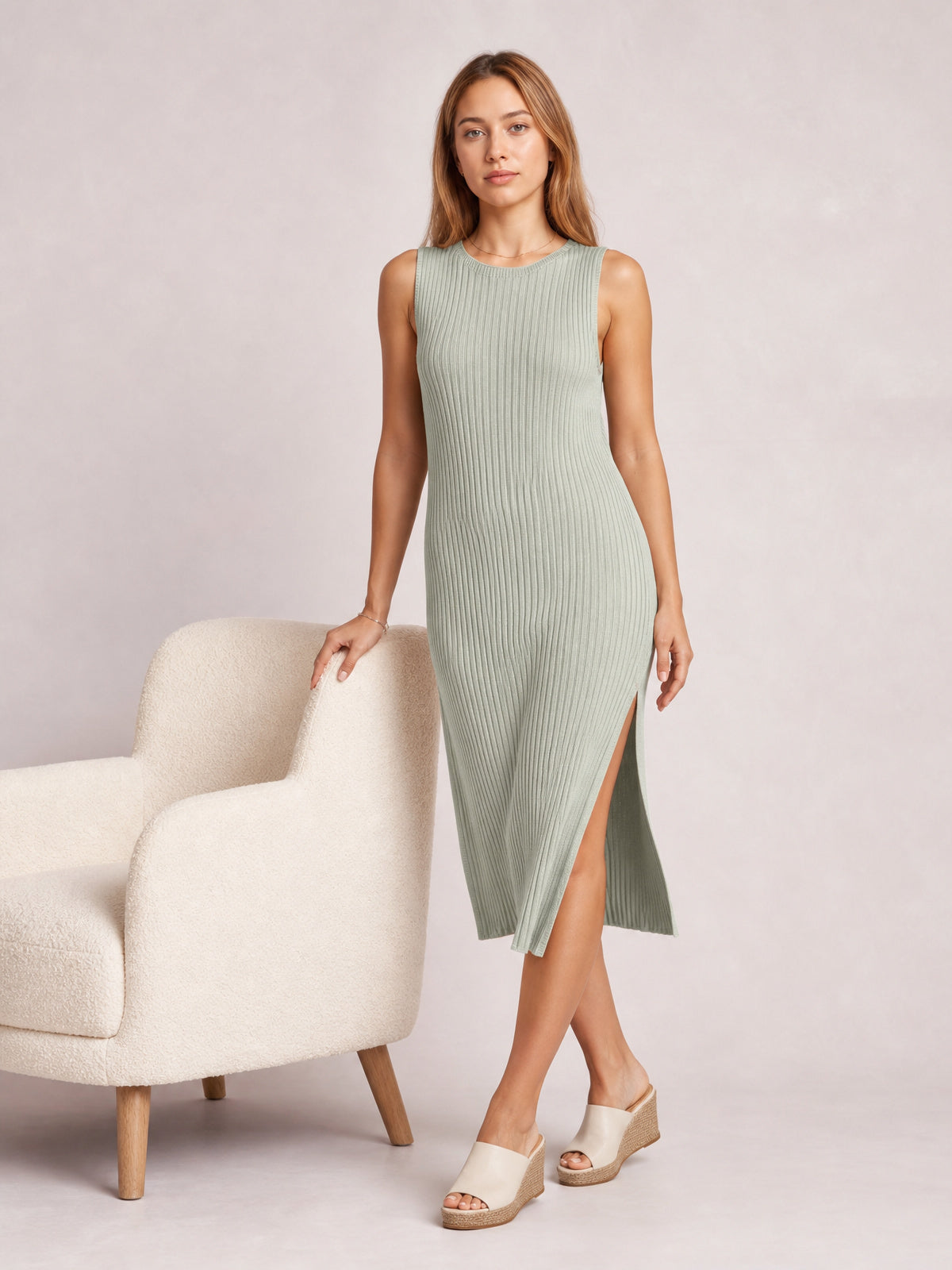 Model poses in a light sage Split Round Neck Sleeveless Dress with vertical ribbing, a body-skimming midi silhouette, and a high side split.