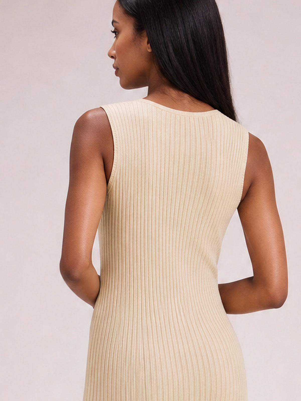 A model poses in profile wearing an ivory sleeveless dress with a rounded neckline, body-skimming silhouette, and fine vertical ribbed texture.