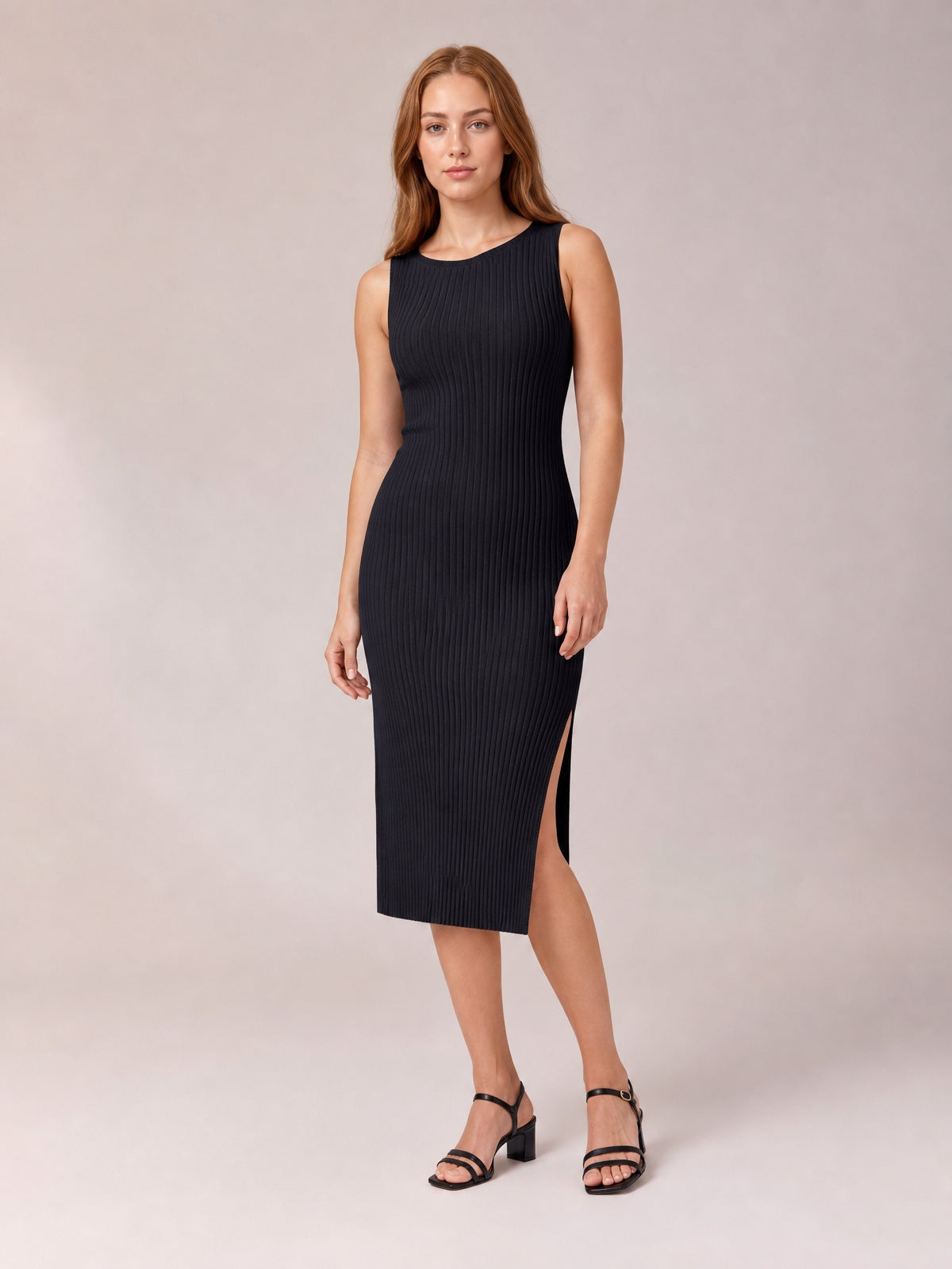 Model poses in a black sleeveless midi dress with a round neck, body-skimming silhouette, vertical ribbed texture, and side split.