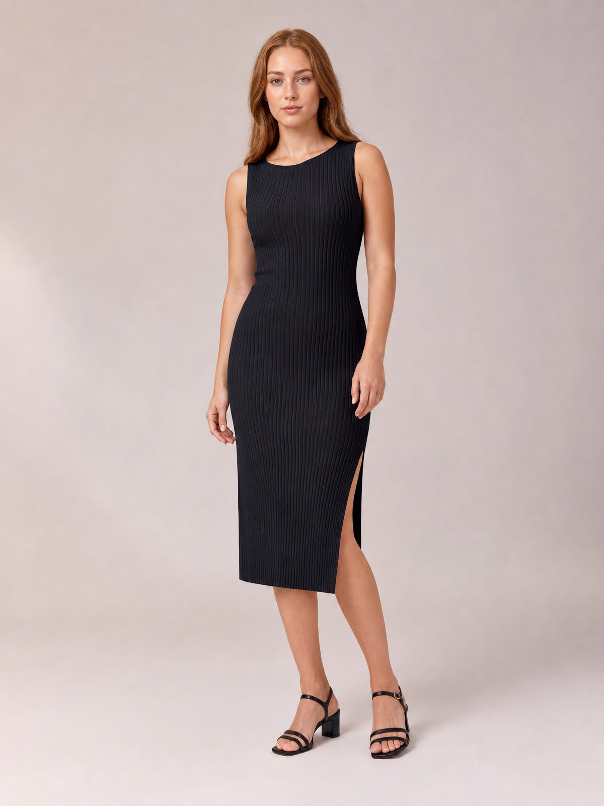 Model poses in a black sleeveless midi dress with a round neck, body-skimming silhouette, vertical ribbed texture, and side split.