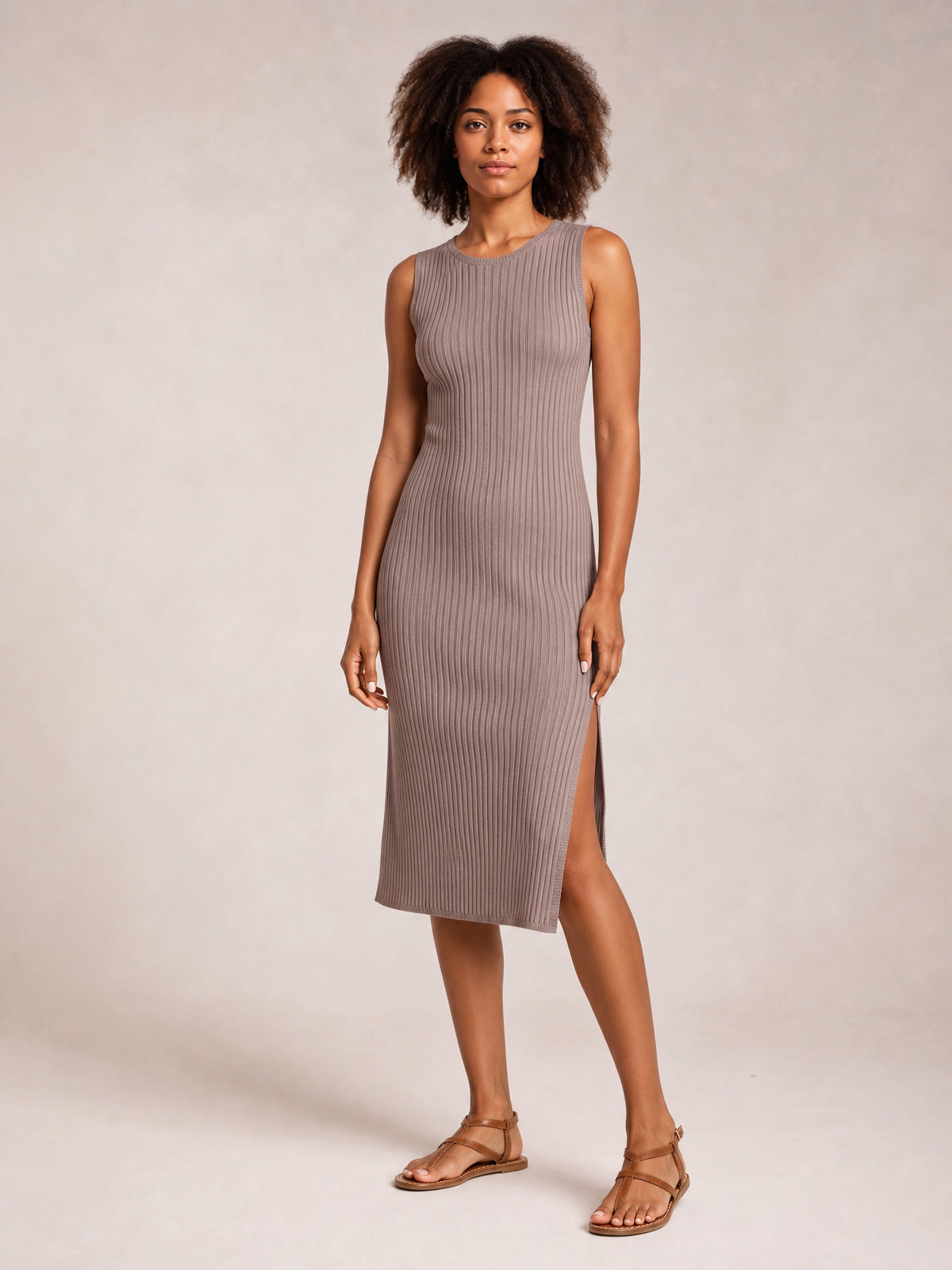Model in a taupe sleeveless midi dress with a round neck, vertical ribbed texture, body-skimming silhouette, and side split, standing in flat sandals.