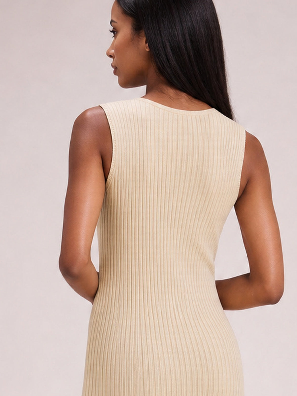 A model poses in profile wearing an ivory sleeveless dress with a rounded neckline, body-skimming silhouette, and fine vertical ribbed texture.