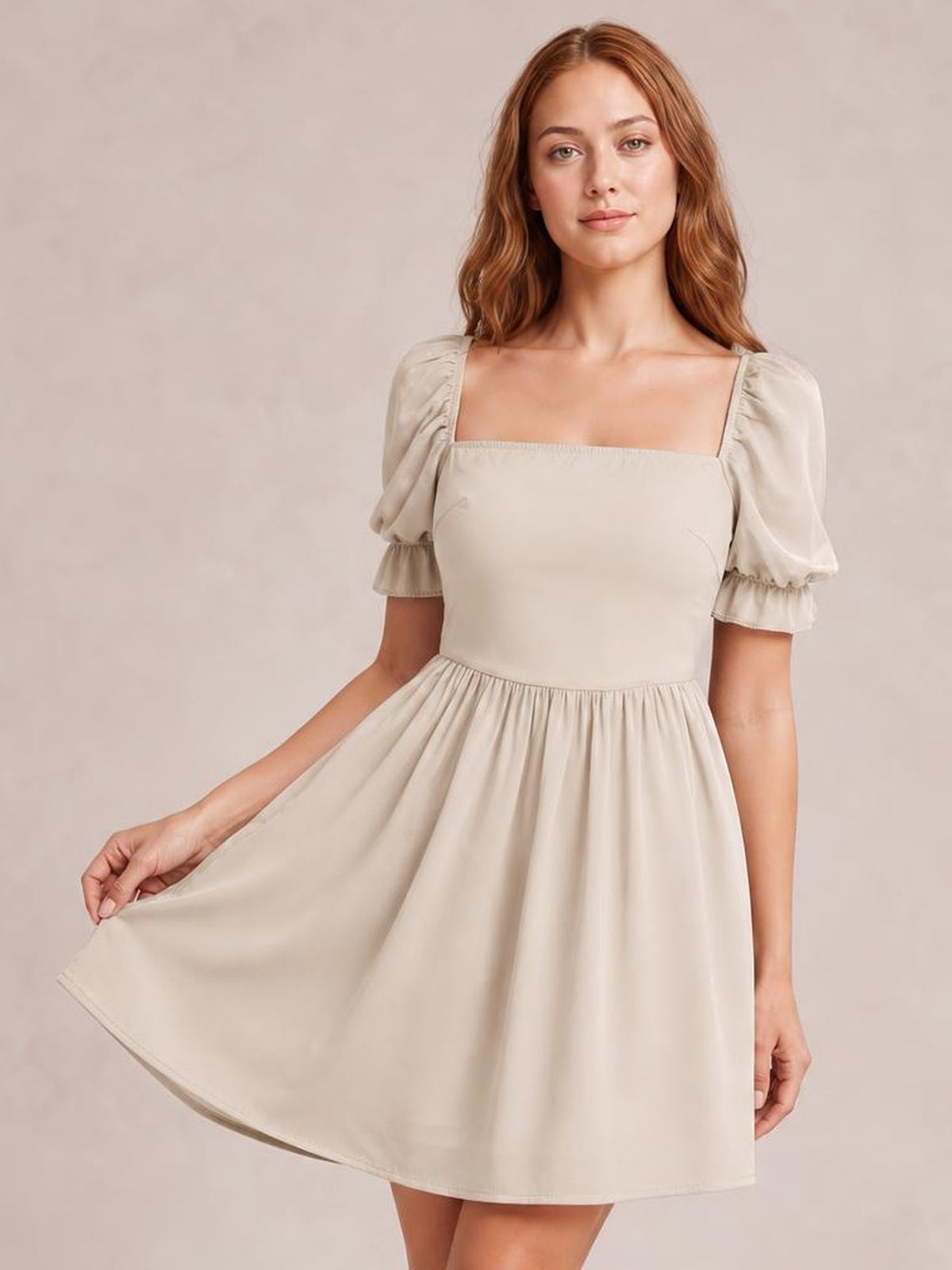 A model holds the hem of a cream square neck mini dress with puffed flounce sleeves, fitted bodice, gathered waist, and flowing A-line silhouette.