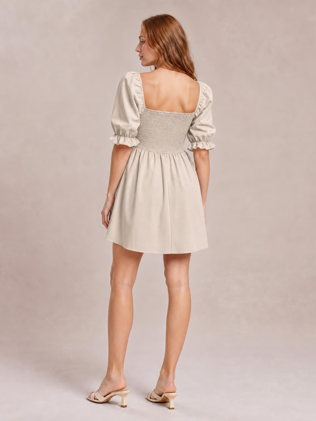 A model stands turned away in a cream square neck mini dress with puffed flounce sleeves, a smocked bodice, and a softly flared skirt.