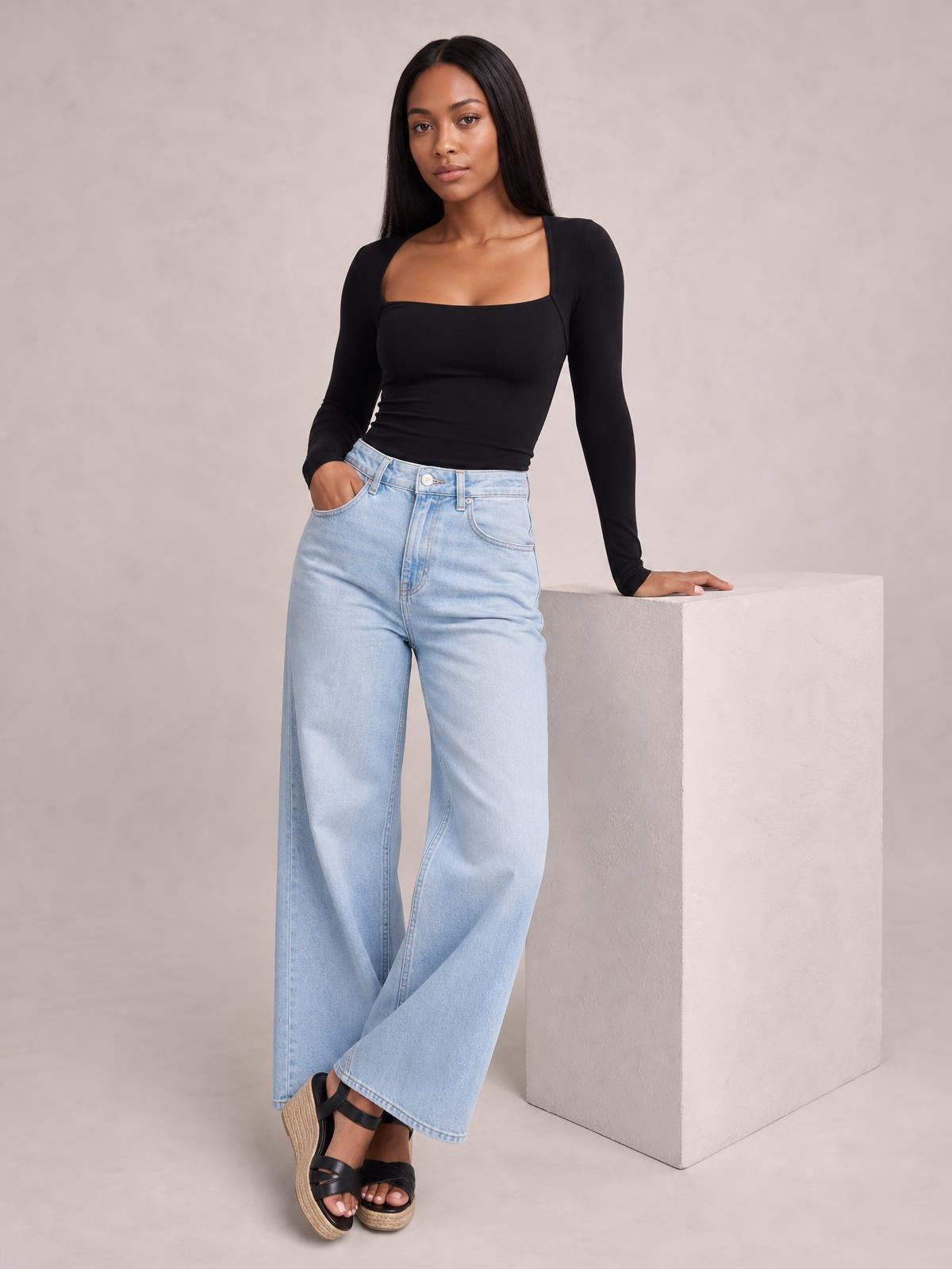 A model wears a black square neck long sleeve T-shirt with a fitted silhouette and moderate stretch, posing with one hand in her jeans pocket.